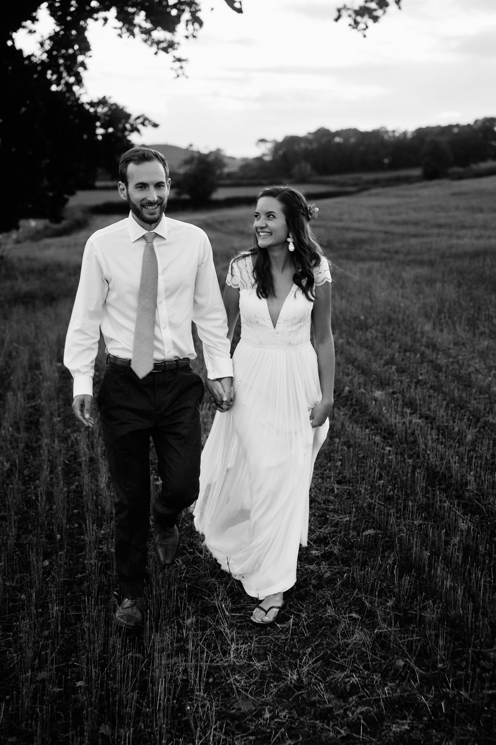 A black and white picture of a couple in their wedding attire walking in a field.