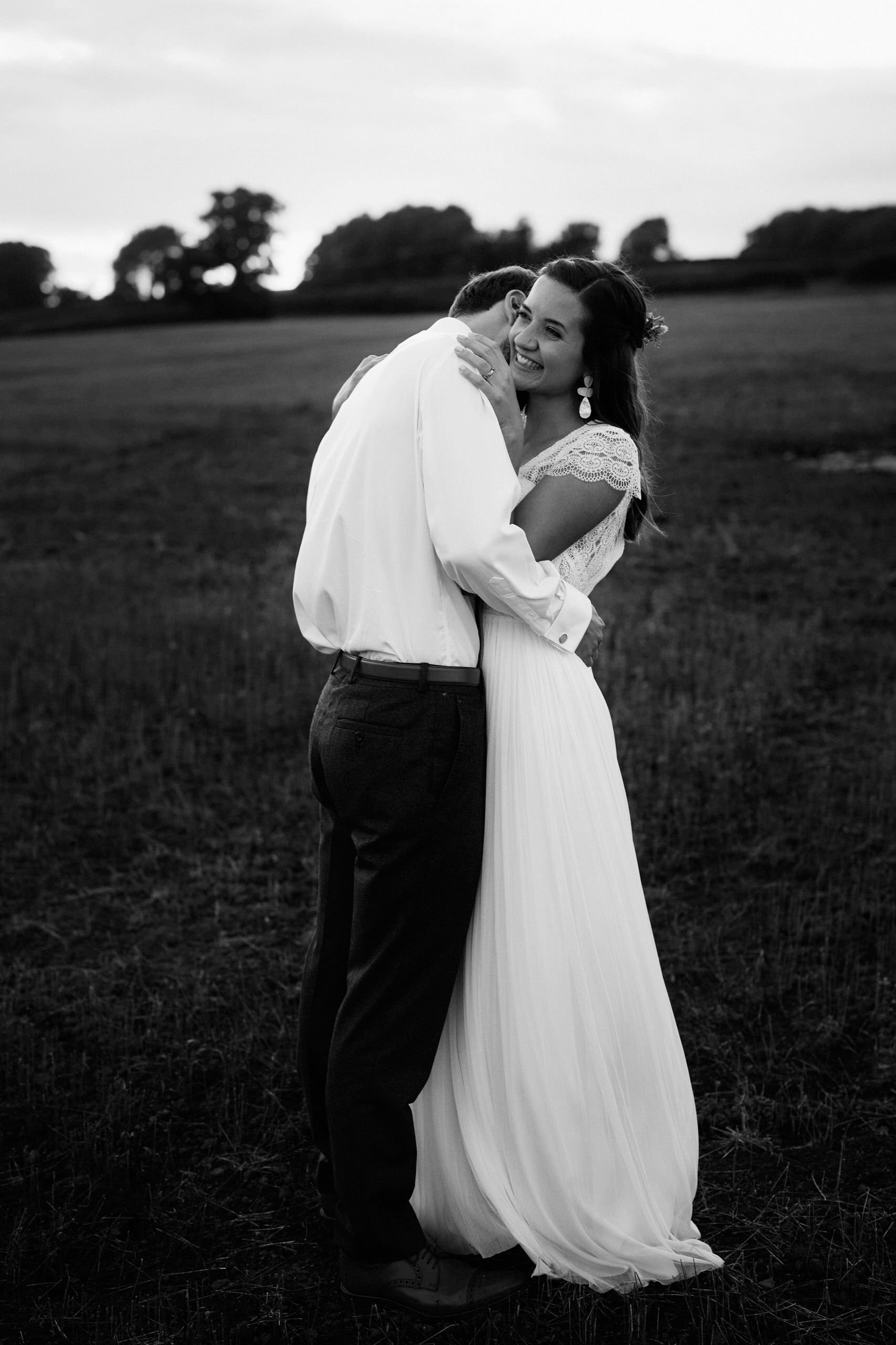 A couple getting married is embracing in an open field.