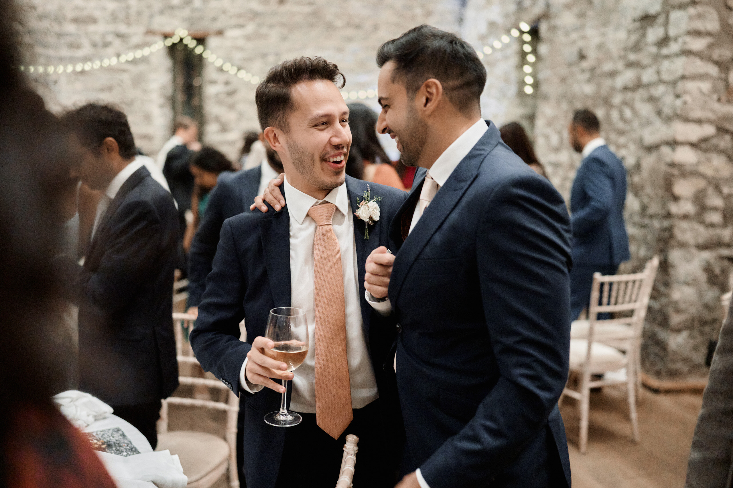 Two guys in suits cracking up at a wedding party.