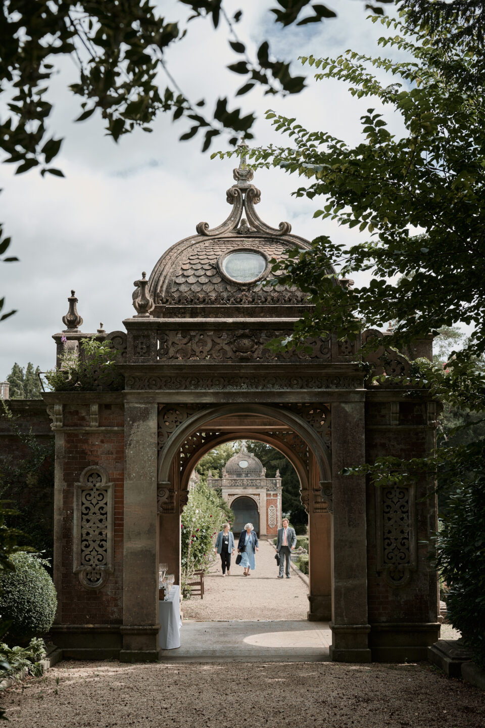 A couple getting married walks through a fancy gate in a garden.