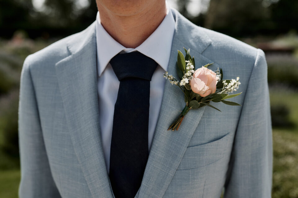 A guy wearing a blue suit with a pink flower pinned on his front.