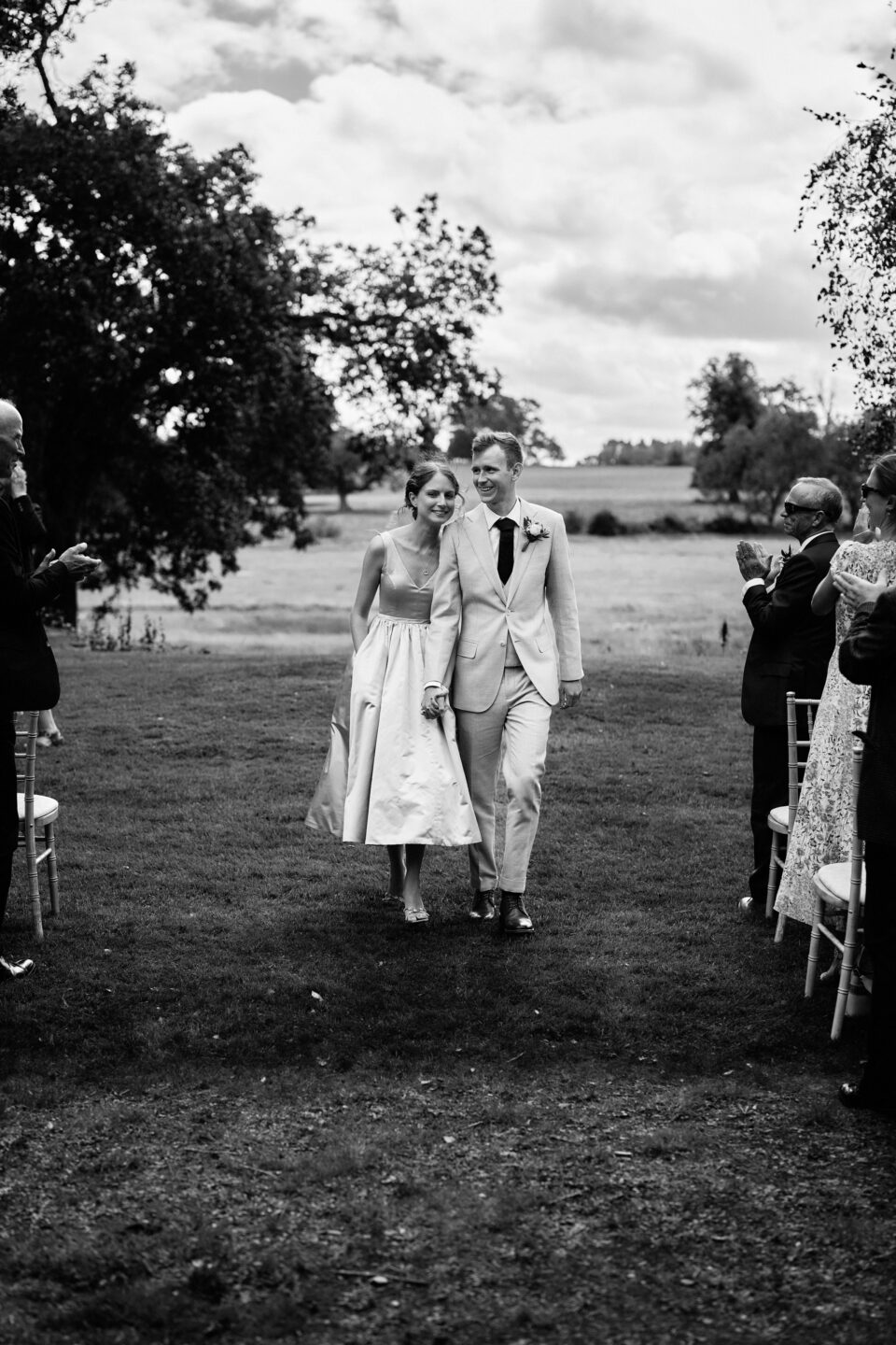 A black and white picture of a couple getting married, walking down the aisle.