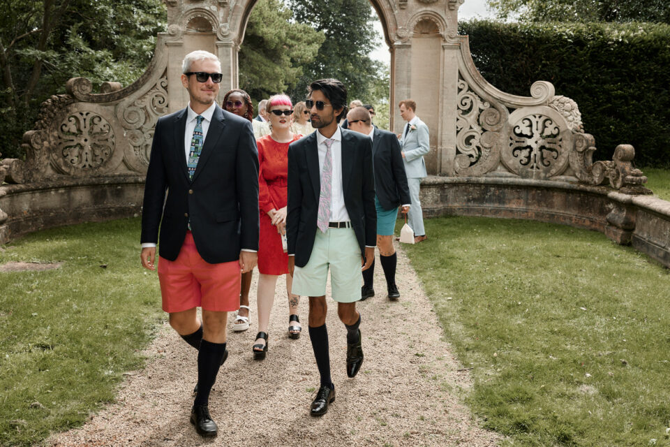 Some guys in suits and shorts are strolling through a garden.