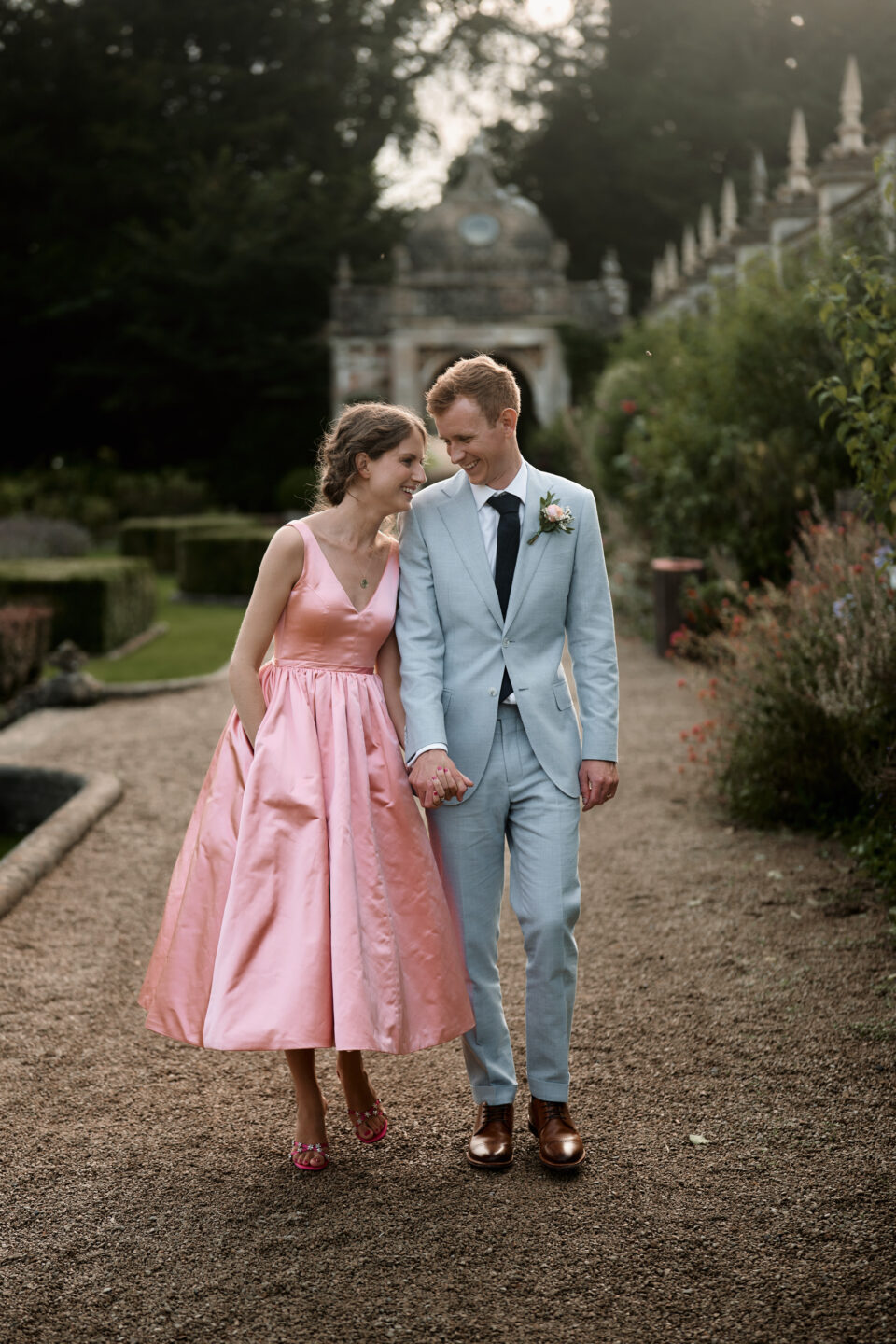 A man and a woman, with the woman wearing a pink dress, are walking down a path. They're getting married.