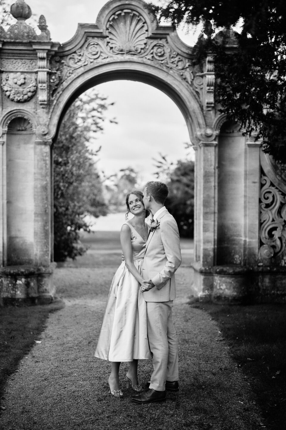 A monochrome picture of a newlywed couple standing before an arch.