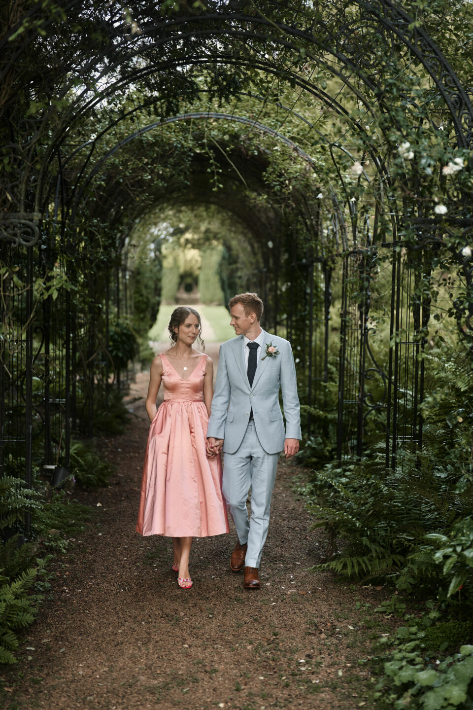 A man and woman getting married are walking under a garden arch.
