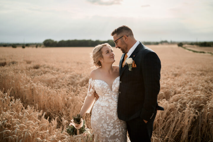 A couple getting married are hugging in a wheat field. The pleasant sunshine is making the scene even better.