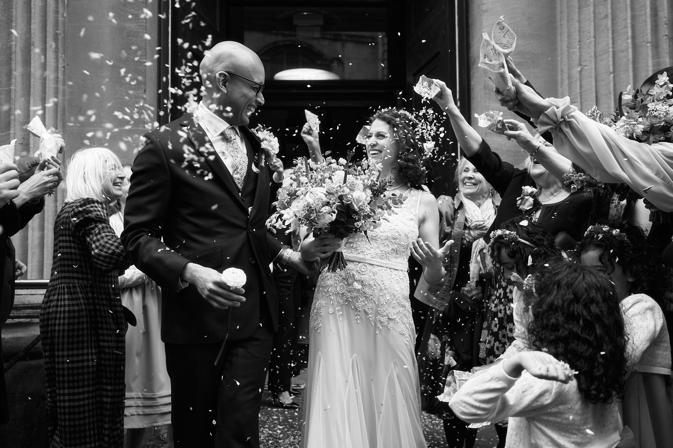 A black and white picture of a bride and groom getting showered with confetti.