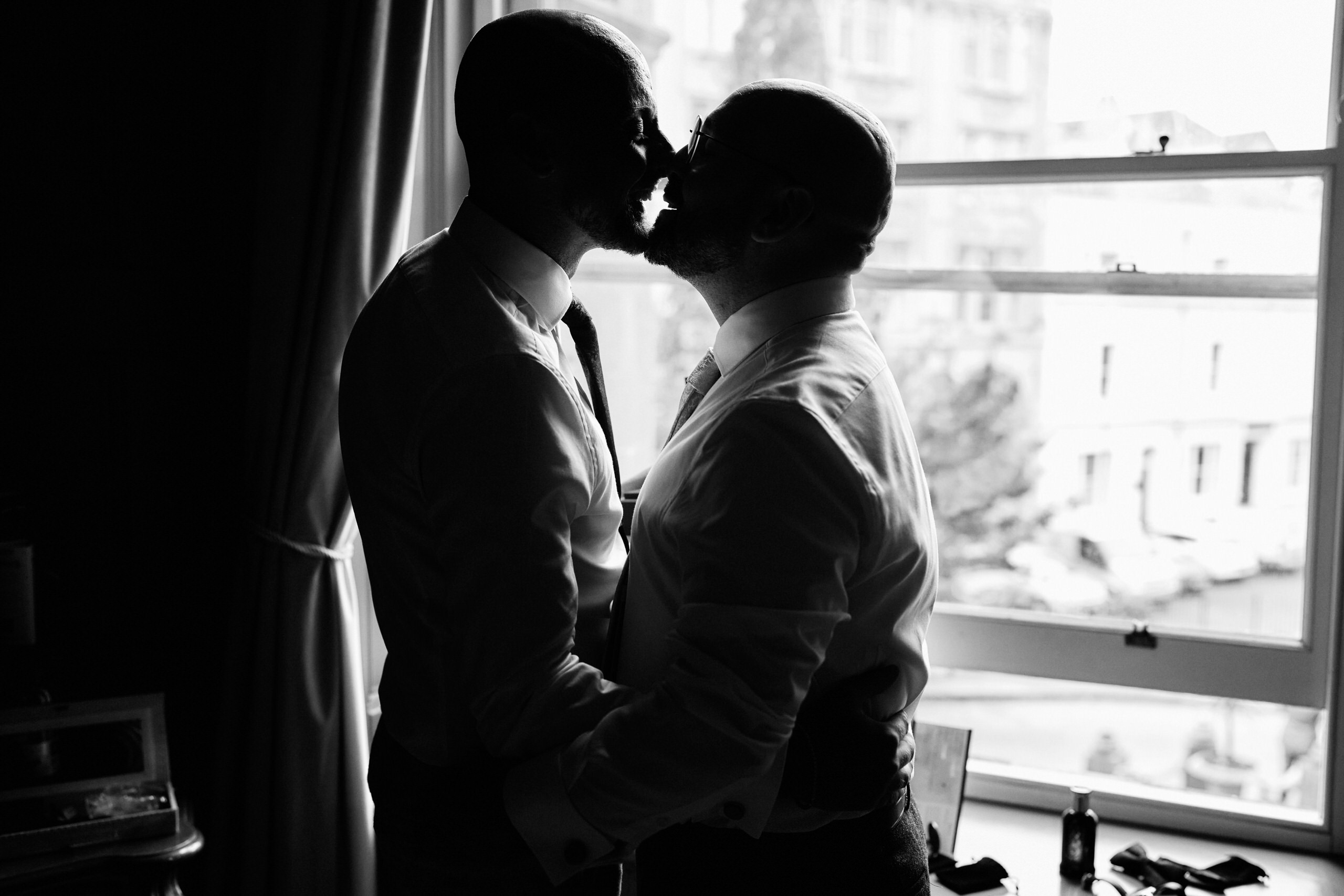 Two guys are smooching by a window.