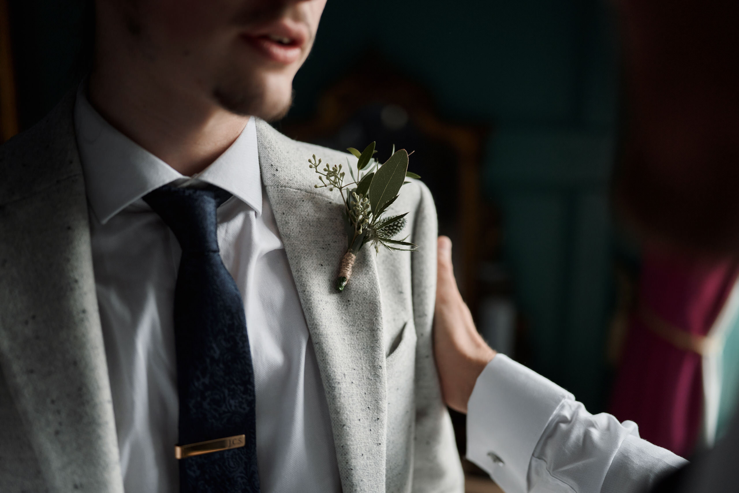 A guy is pinning a flower on a groom.