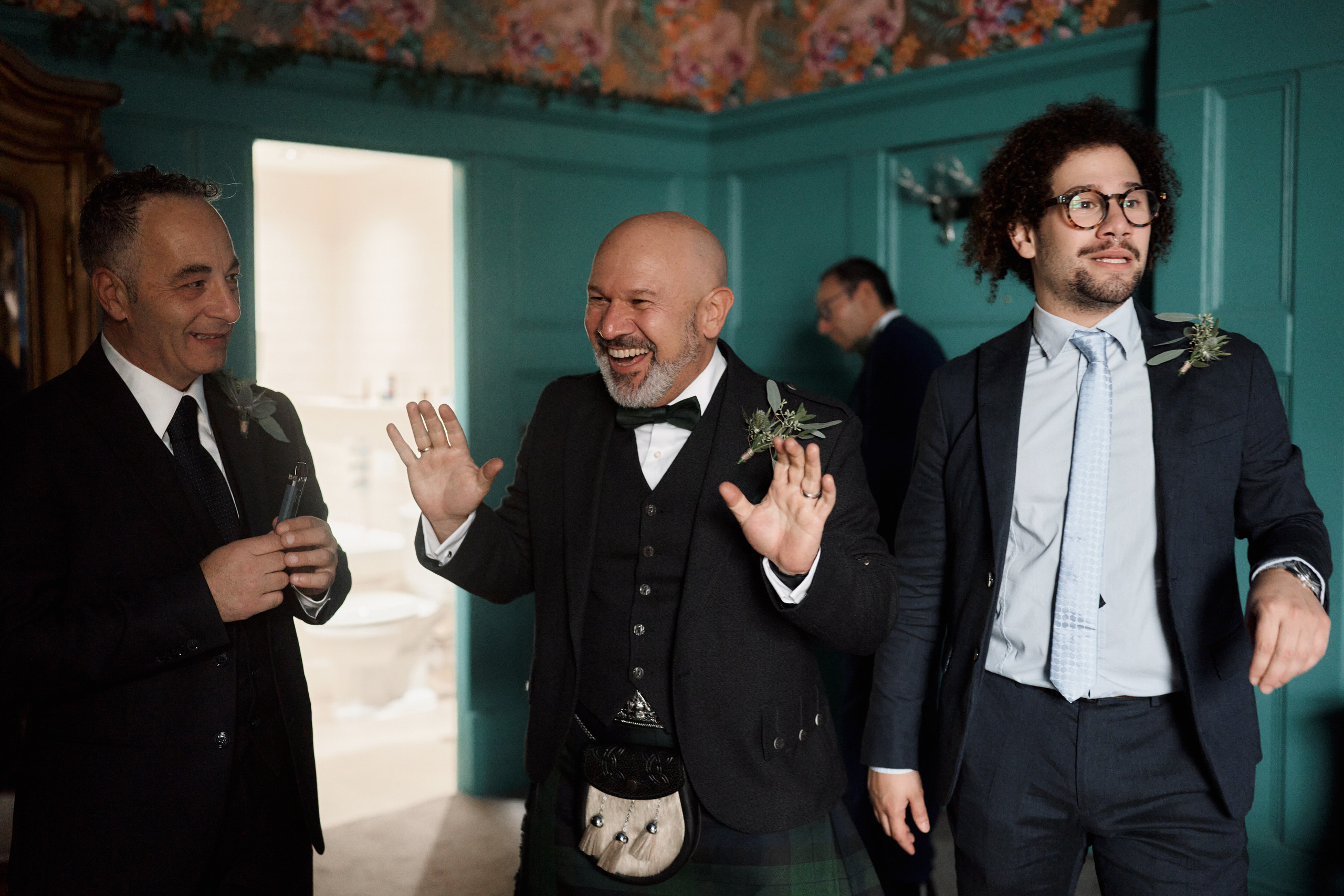 Three guys dressed in suits and kilts are in a room.