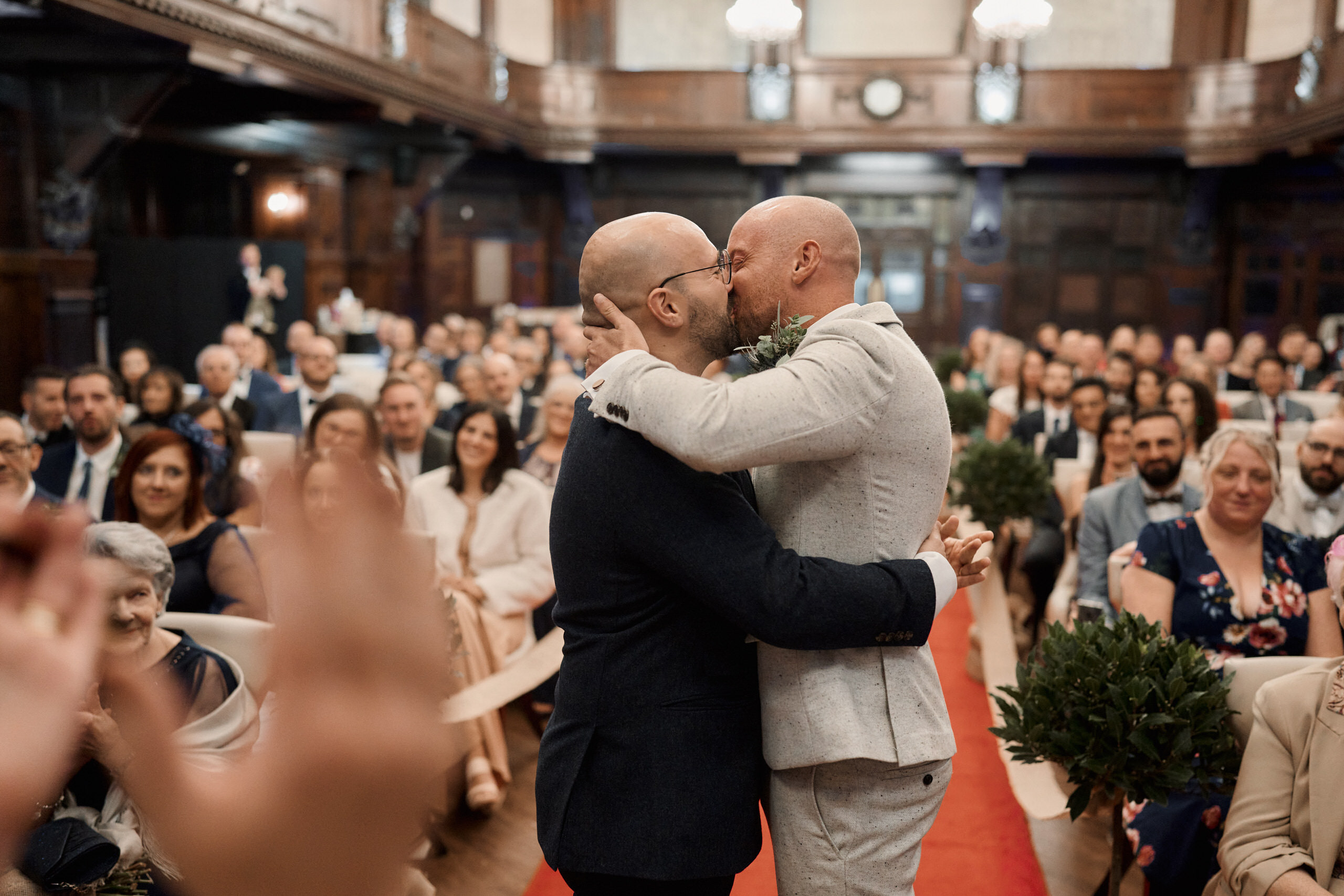 A guy kisses another guy at a wedding.