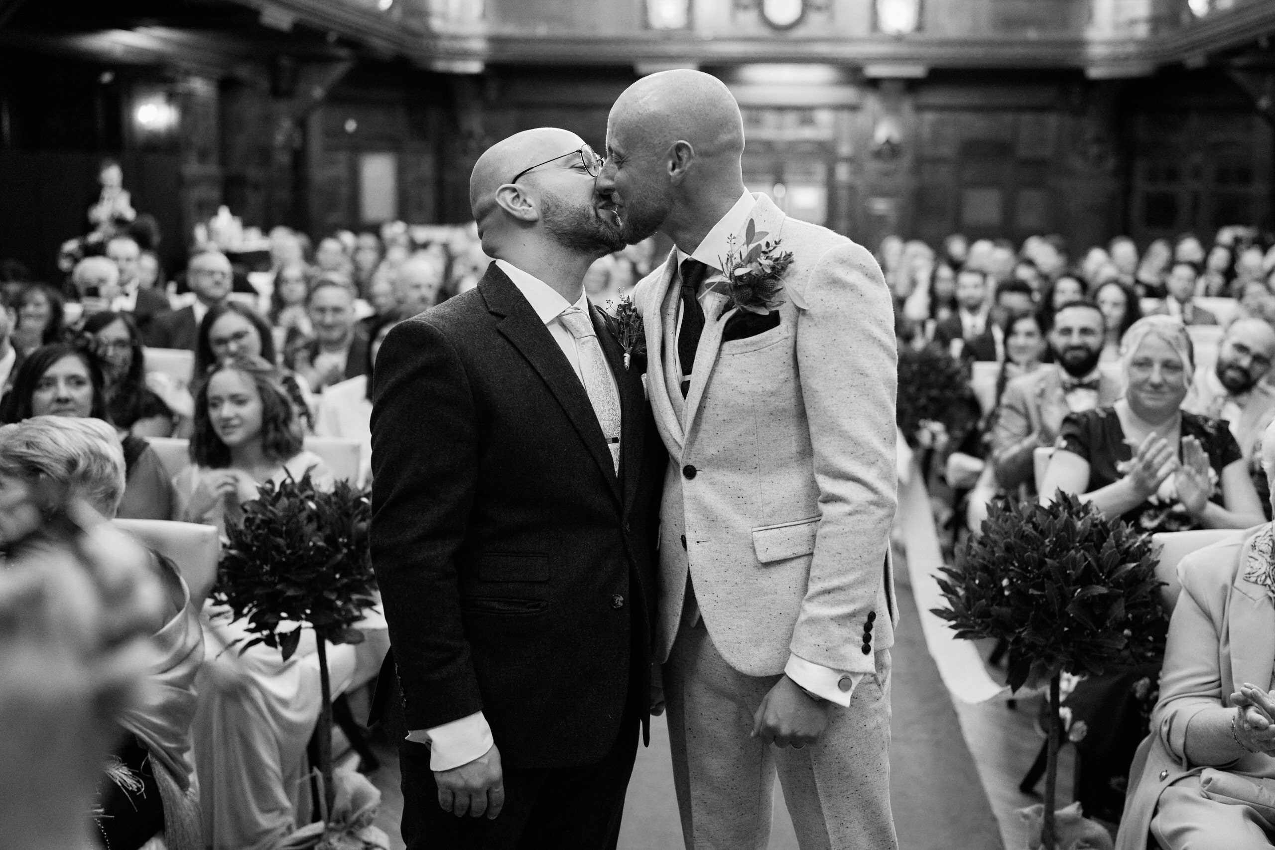 A black and white picture of two guys kissing at a wedding.