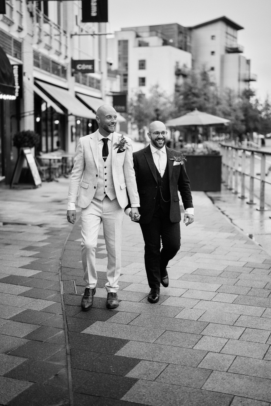 Two guys dressed in suits are strolling down the pavement.
