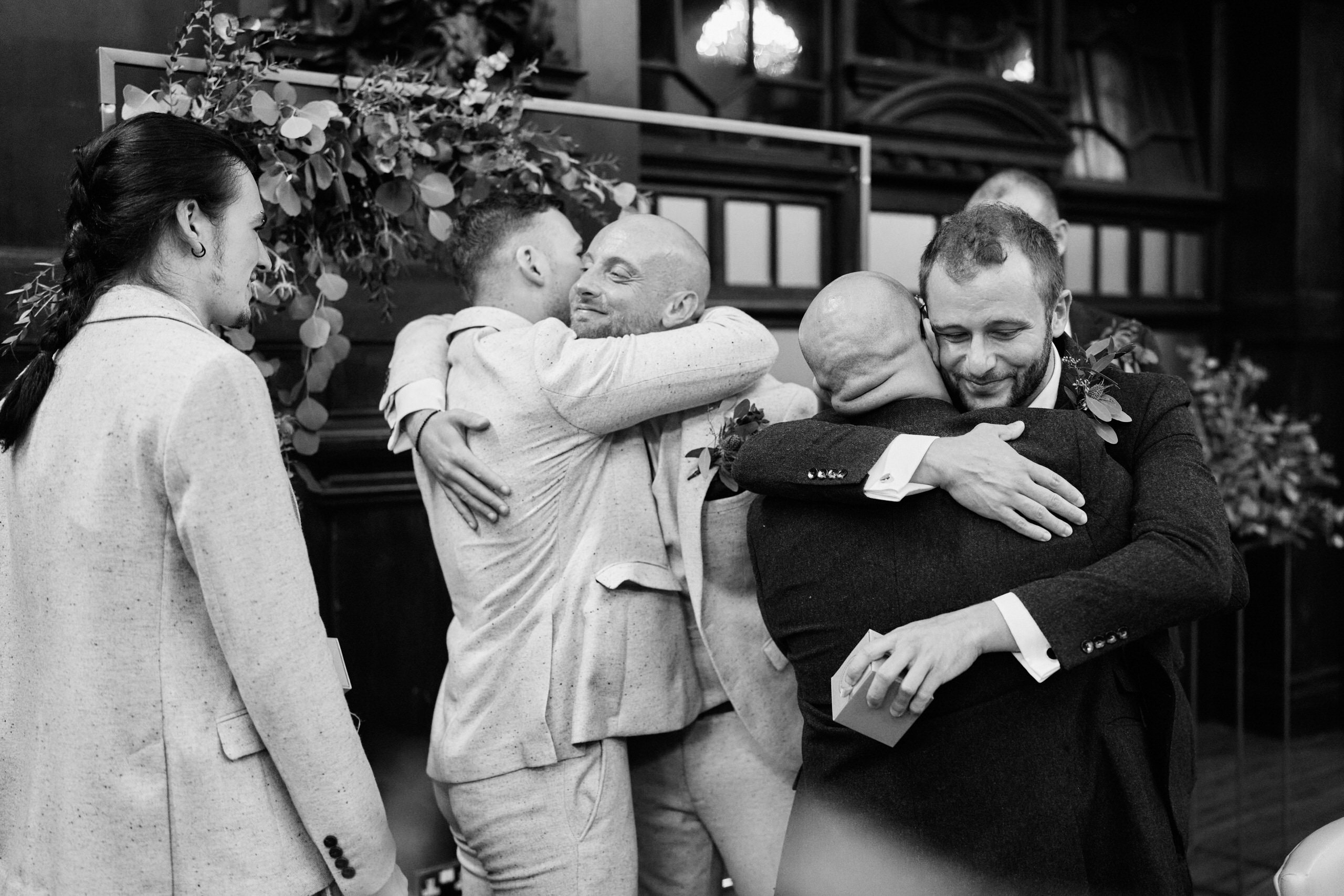 A bunch of guys are giving each other hugs at a wedding.