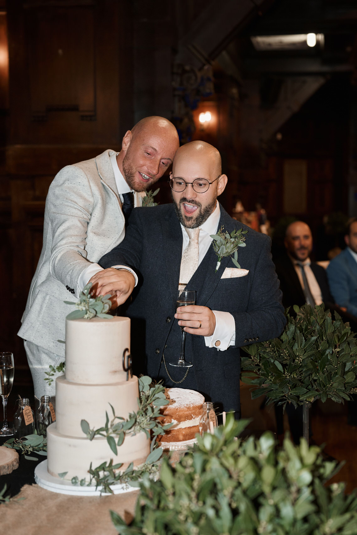 Two guys slicing a wedding cake.