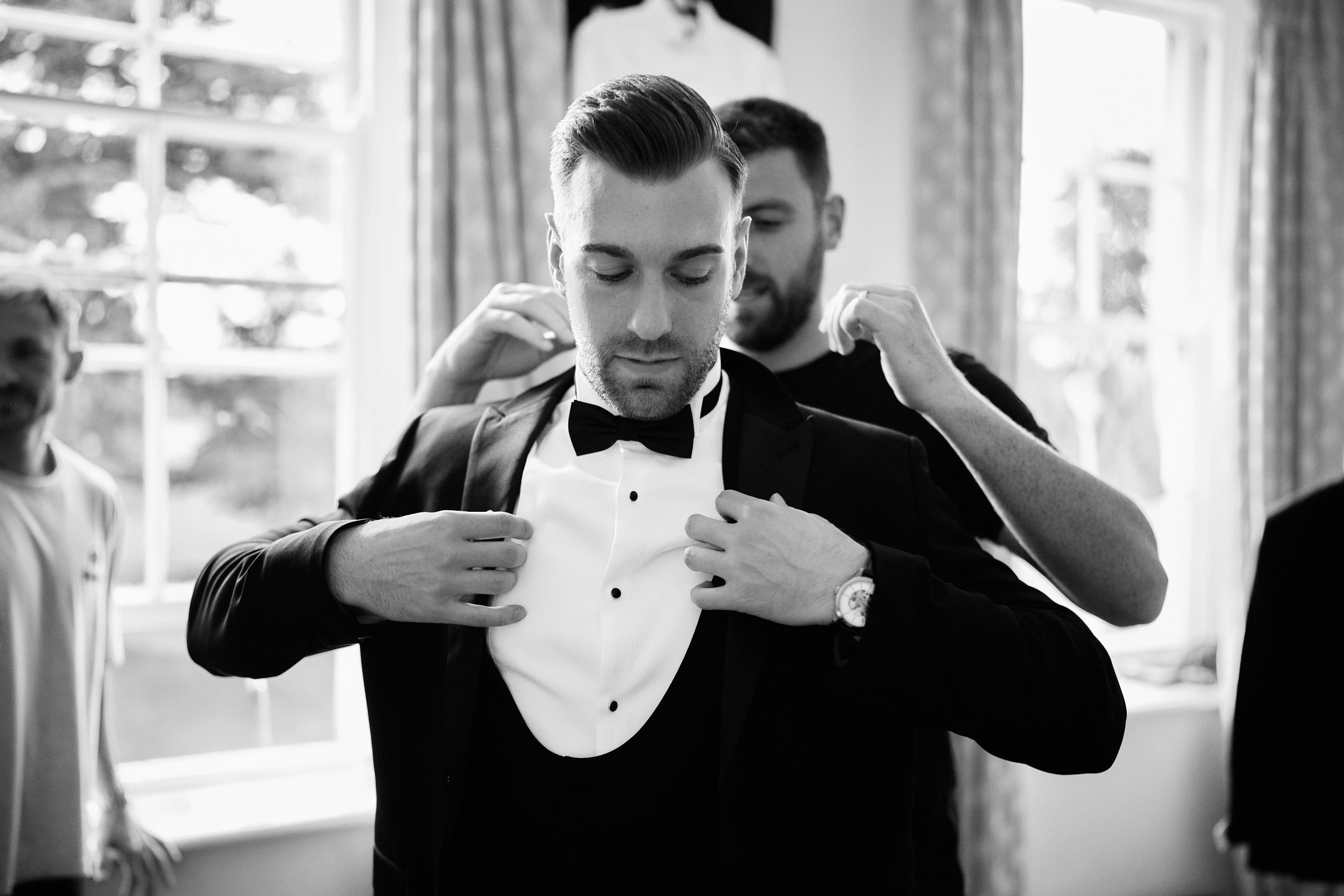 A man in a tuxedo is adjusting his tie.