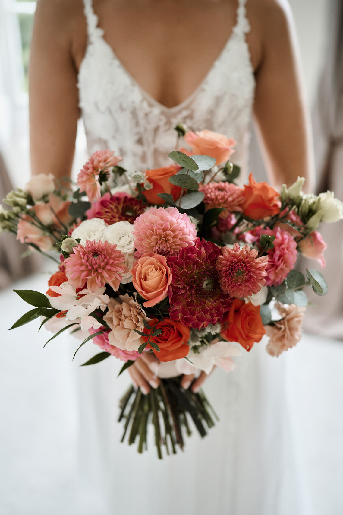 A bride holding a bouquet of pink and orange flowers.