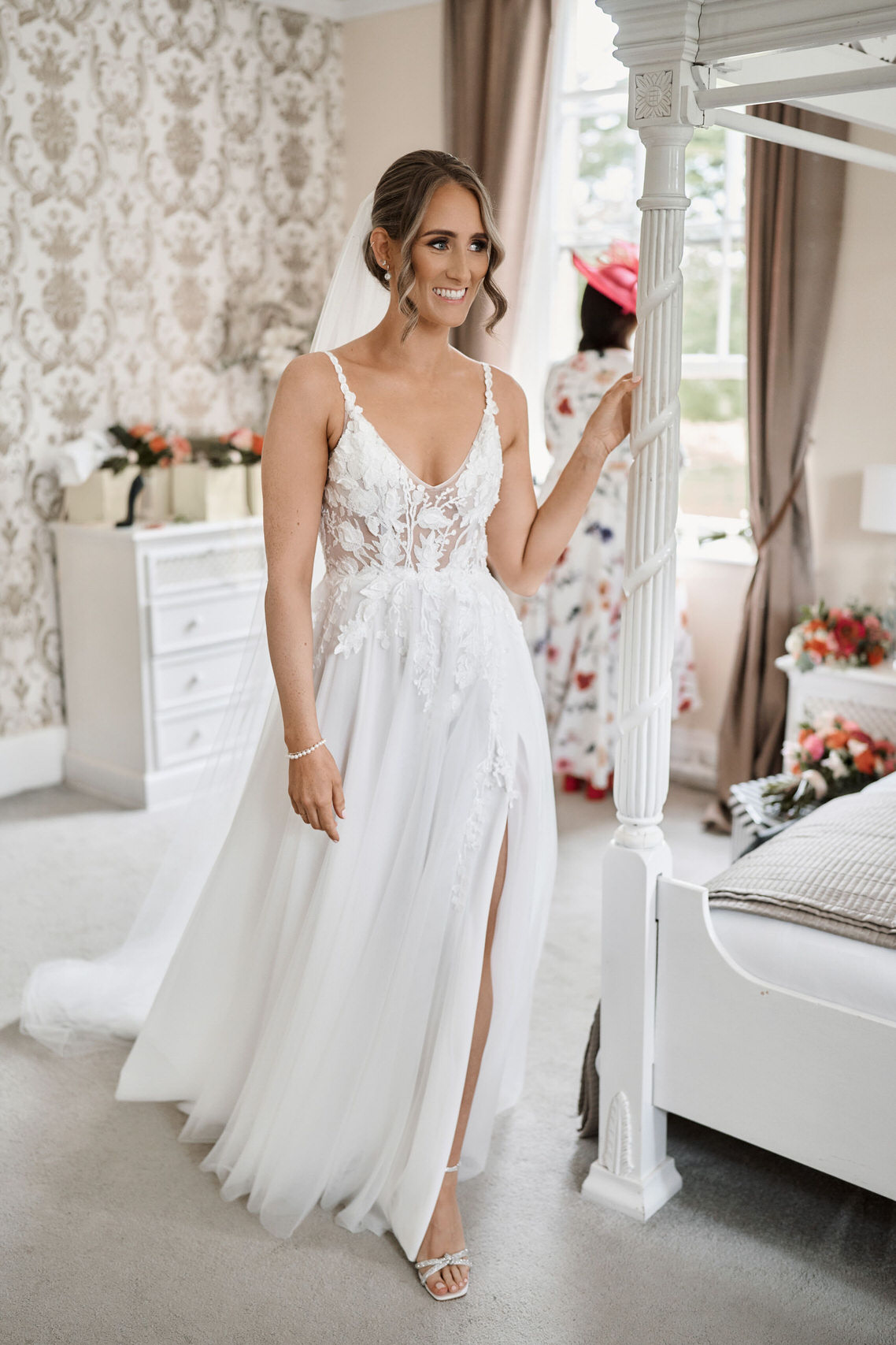 A bride in a white wedding dress standing in front of a four poster bed.