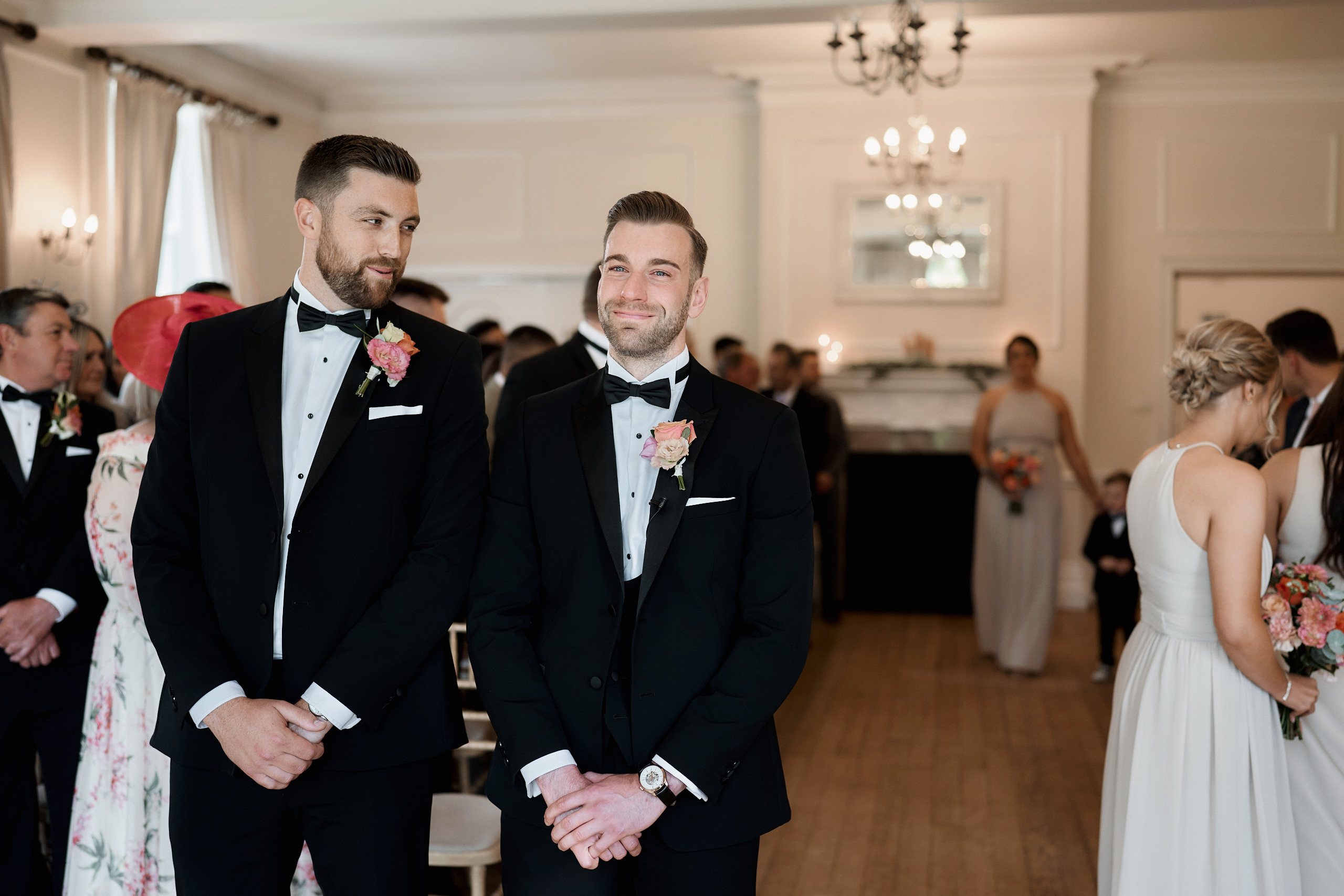 Two grooms in tuxedos walking down the aisle.
