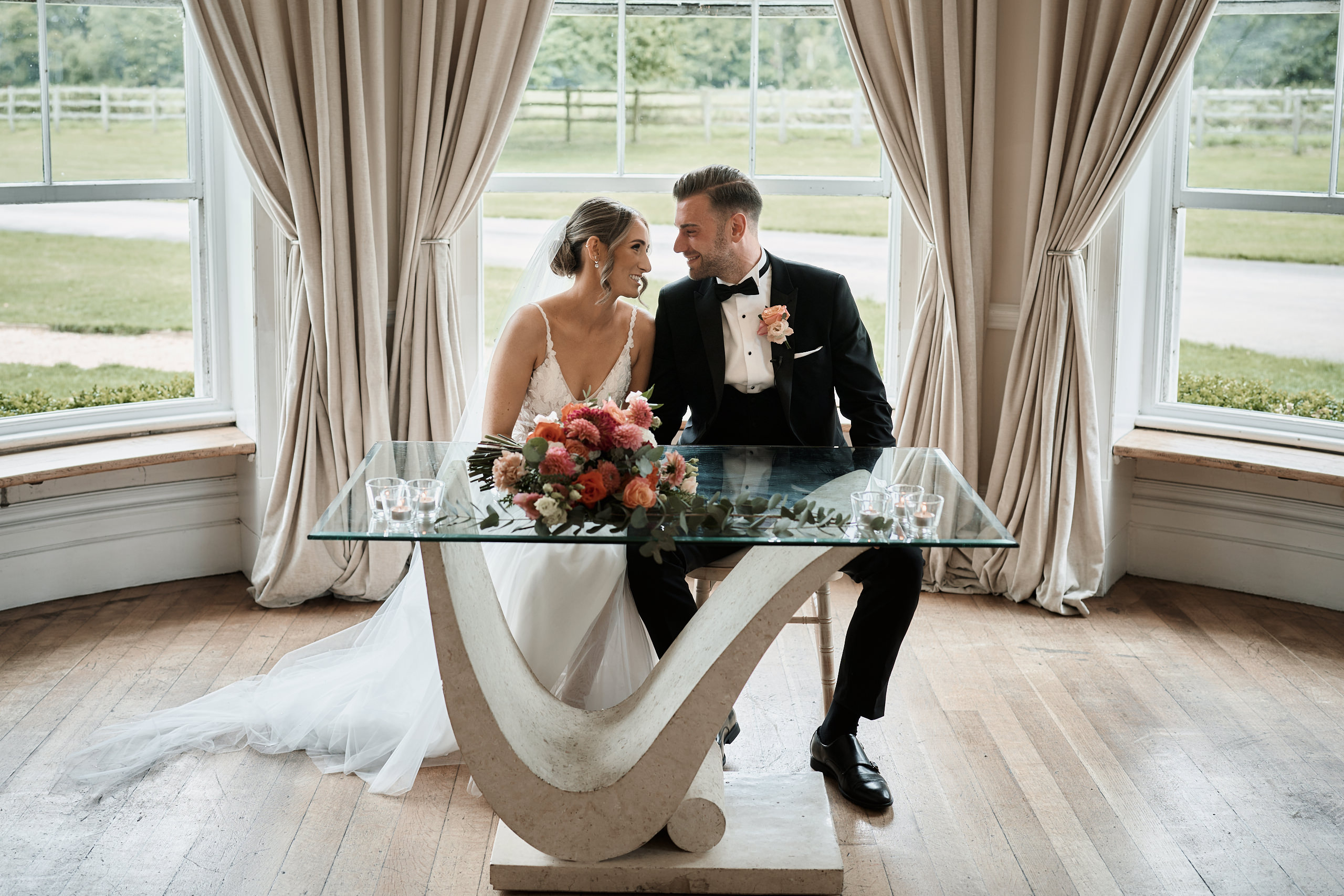 A bride and groom sitting at a table in a room with large windows.