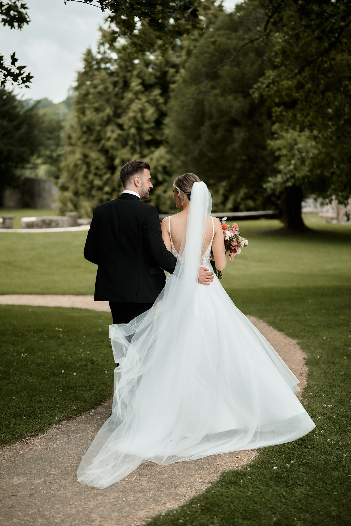 A bride and groom walking down a path in a park.