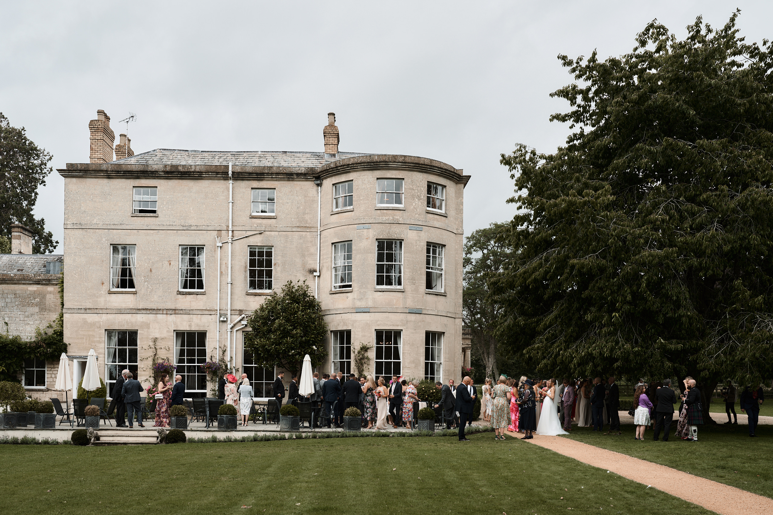 A wedding party standing in front of a large mansion.