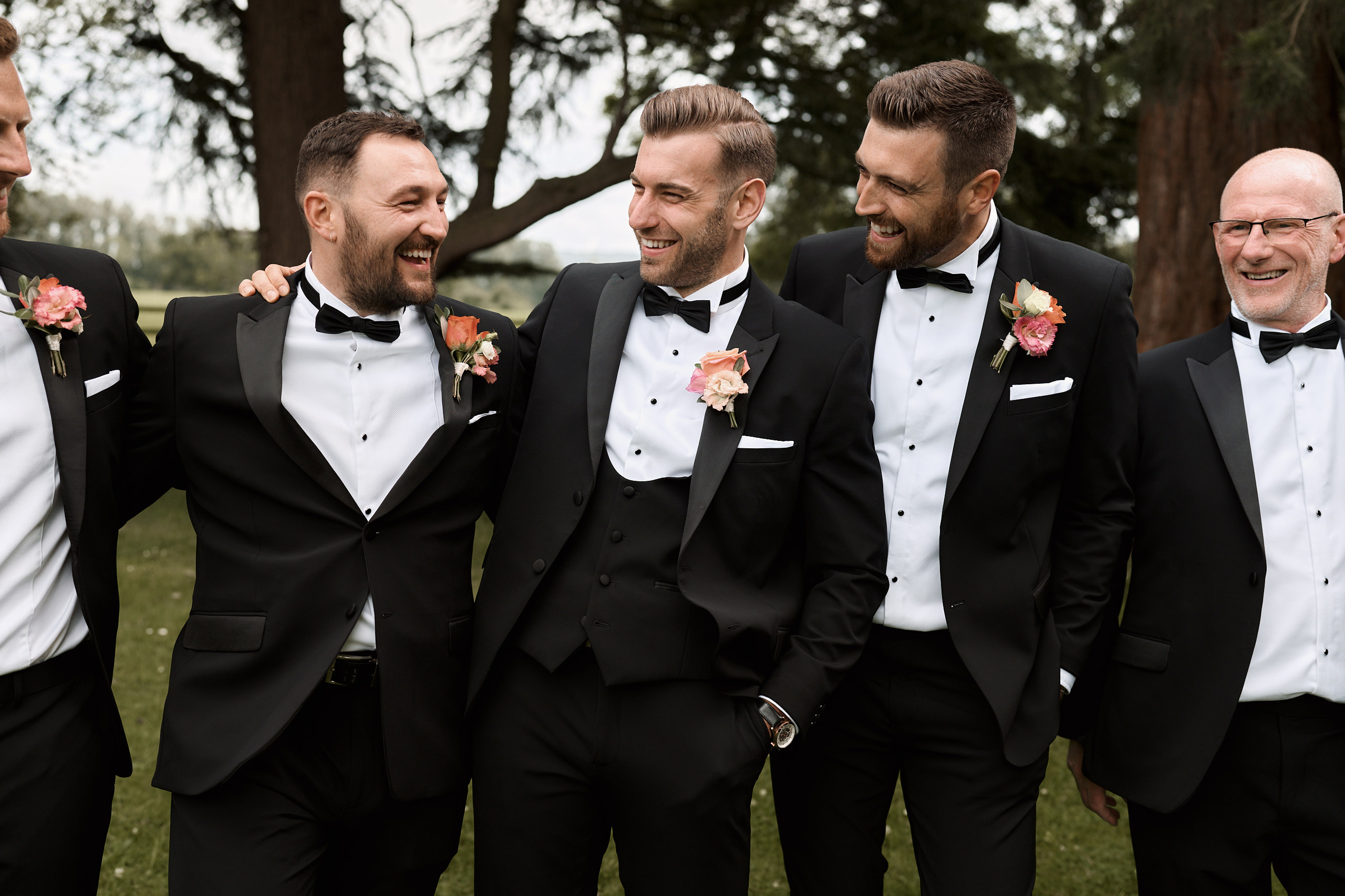 A group of groomsmen in tuxedos laughing together.