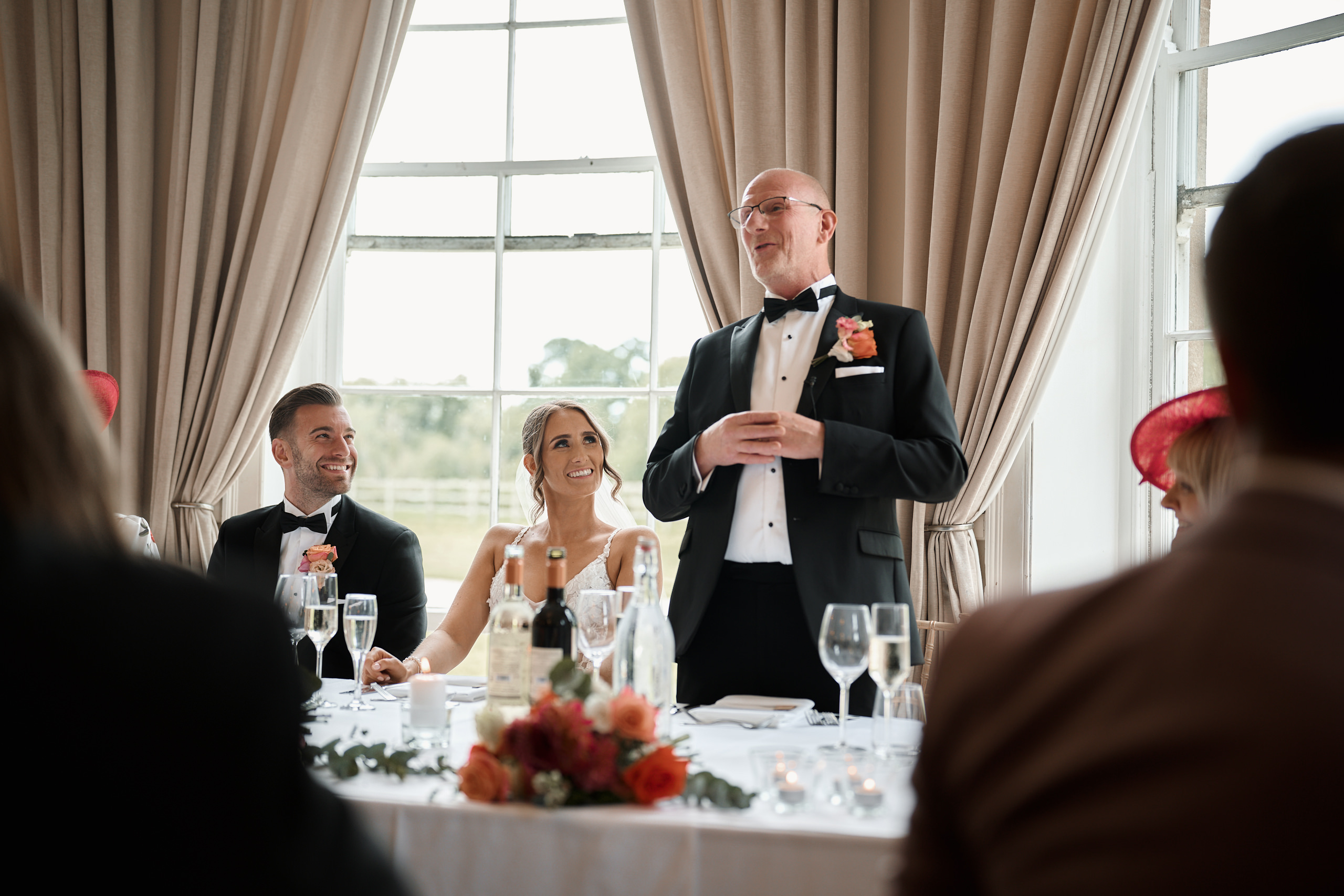 A man in a tuxedo giving a speech at a wedding.