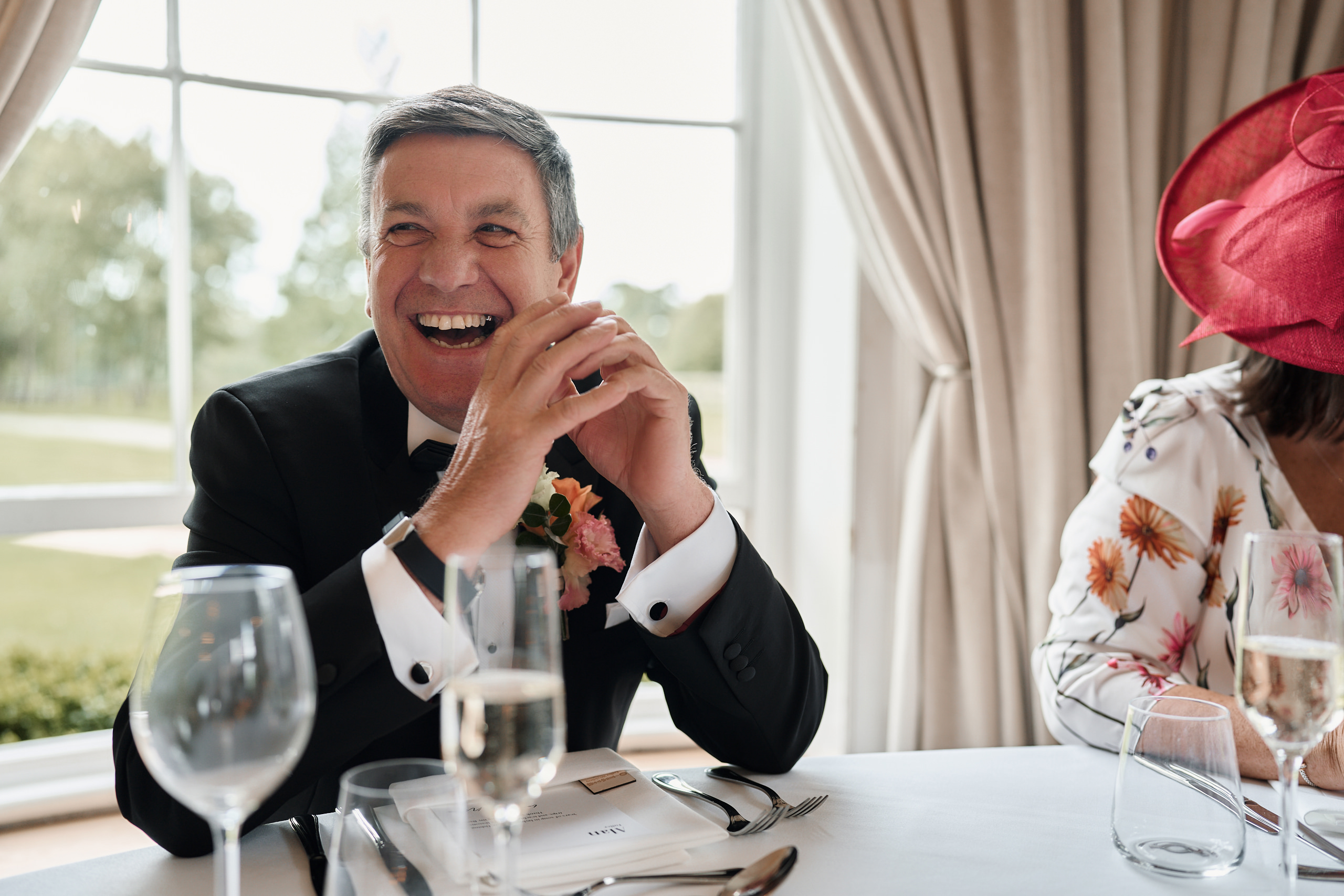 A man in a tuxedo laughing at a table.