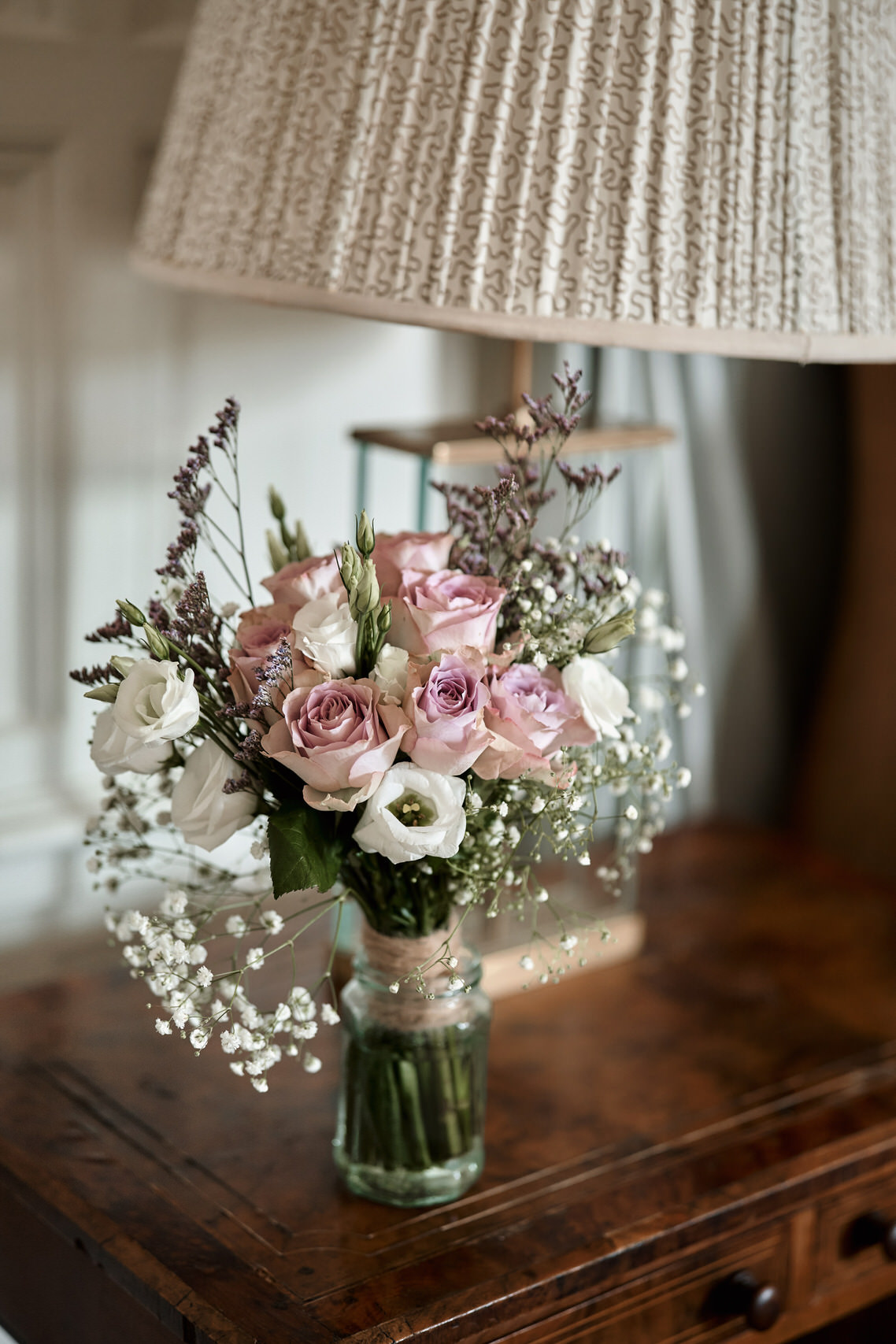 There's a vase with pink and white flowers next to a lamp on a table.