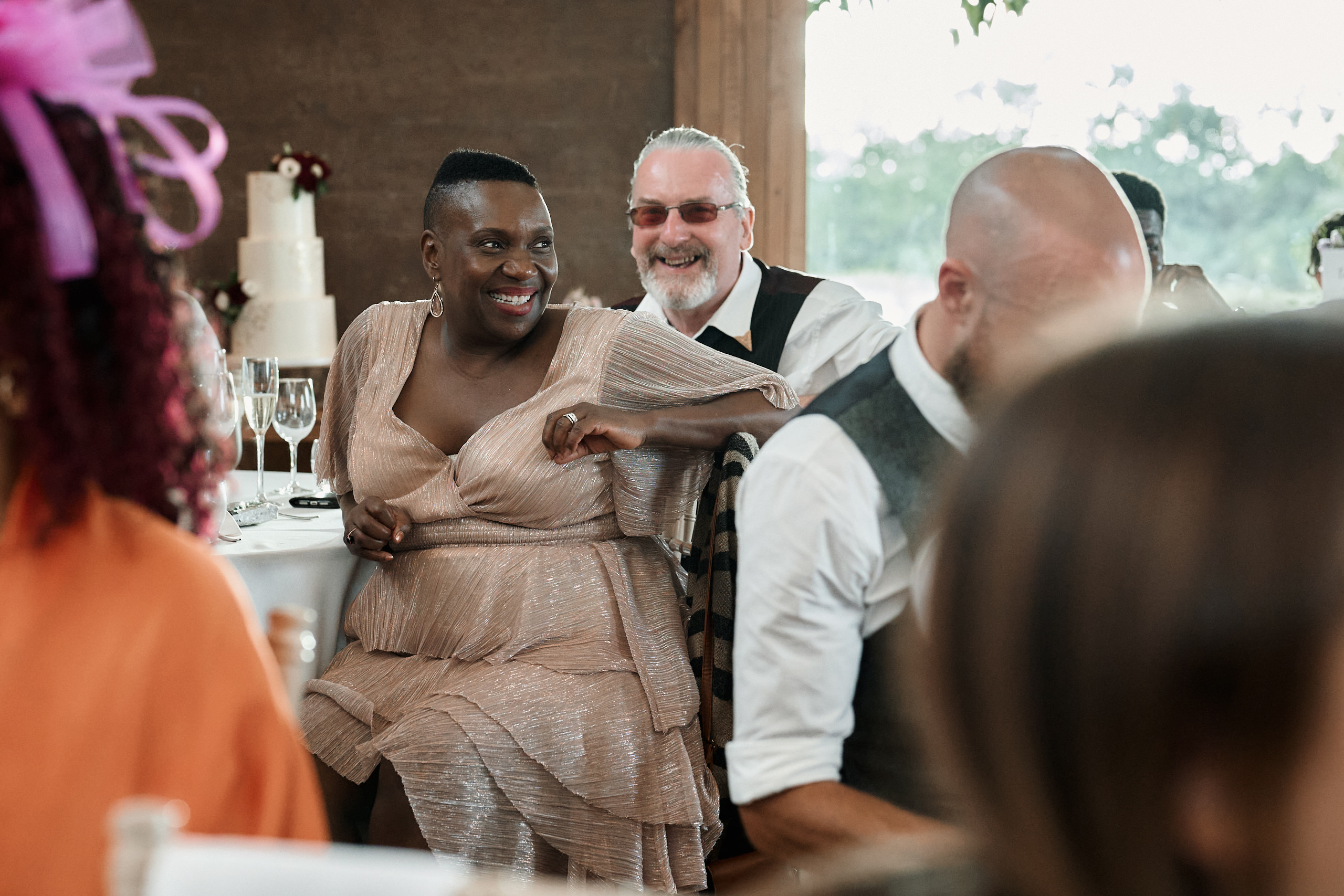 A lady is cracking up as she sits at a table during a wedding.
