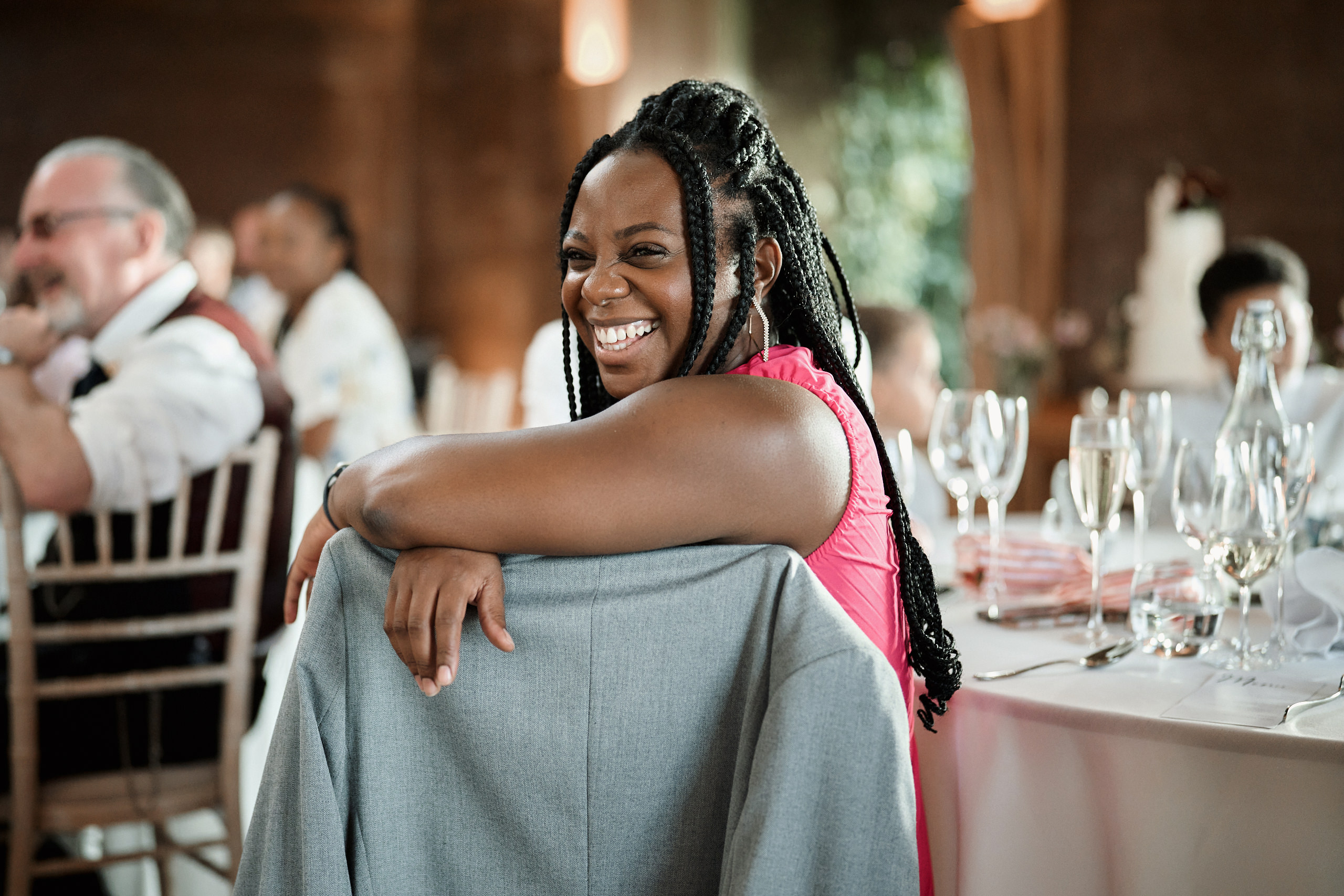 A woman is grinning as she sits at a table during a wedding.