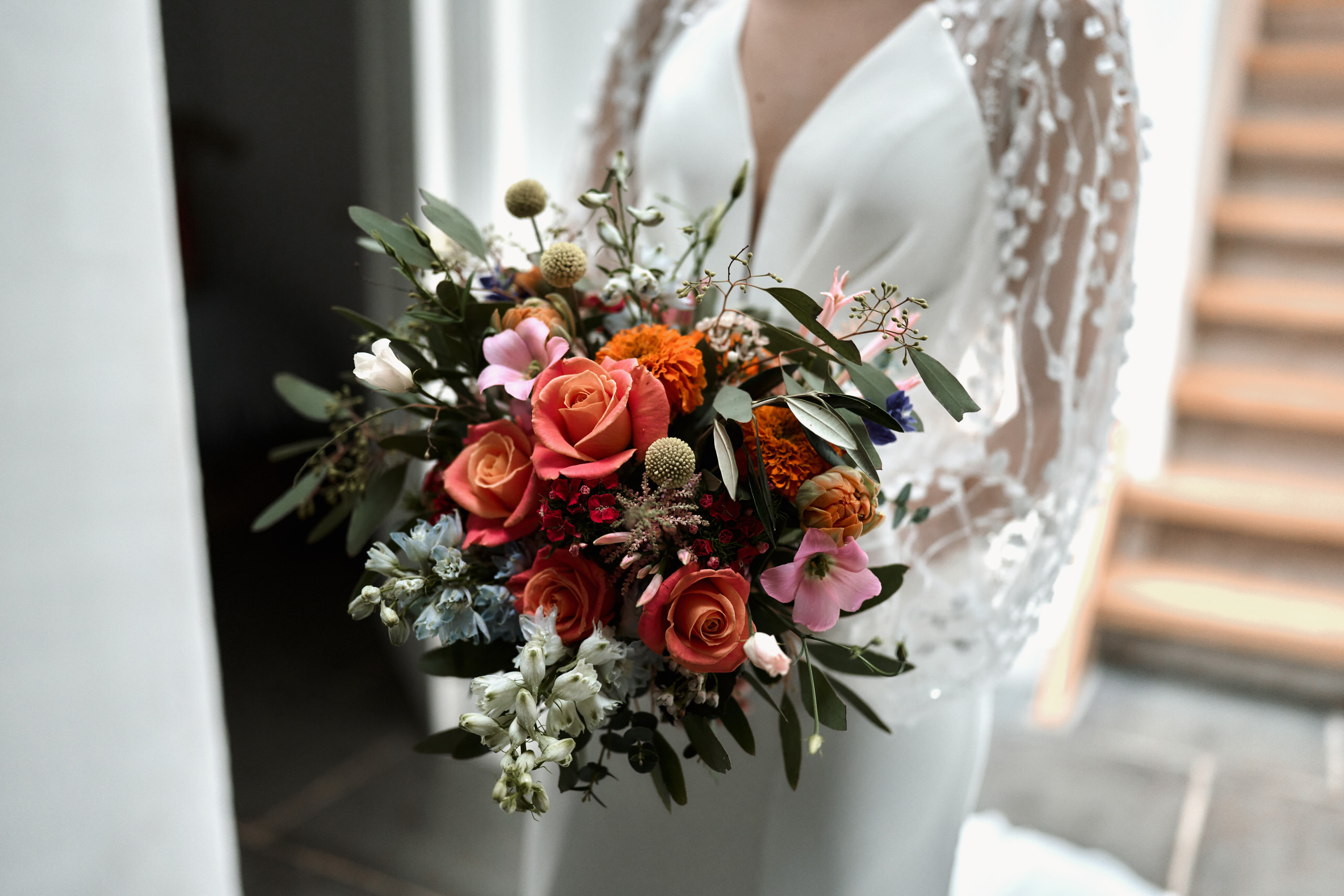 A woman is holding a bunch of flowers in front of some stairs on her wedding day.