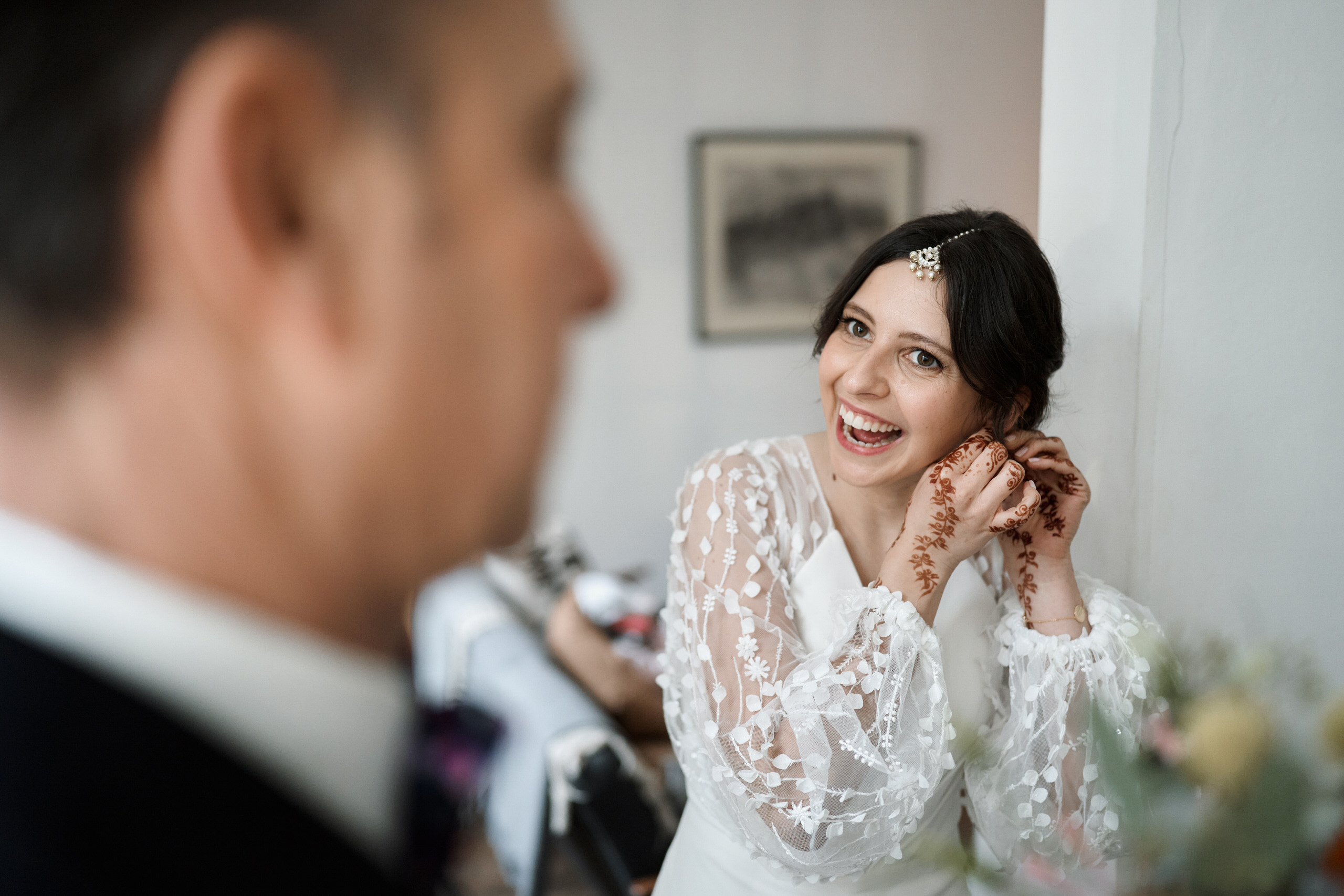 A bride is grinning as she looks at herself in the mirror.