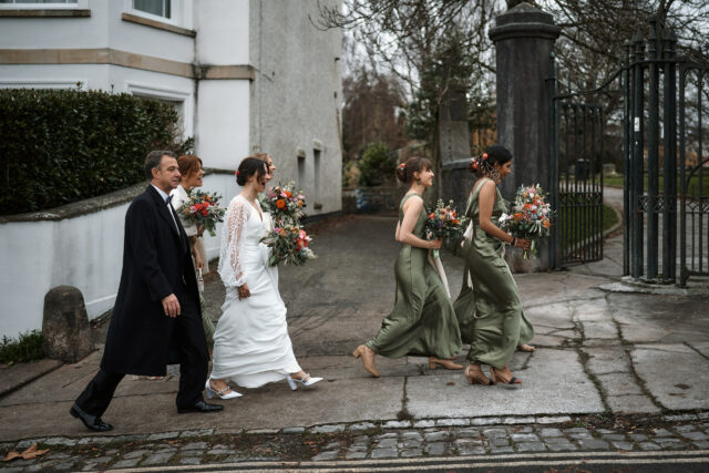 A bride and her bridesmaids are strolling down a street paved with cobblestones.