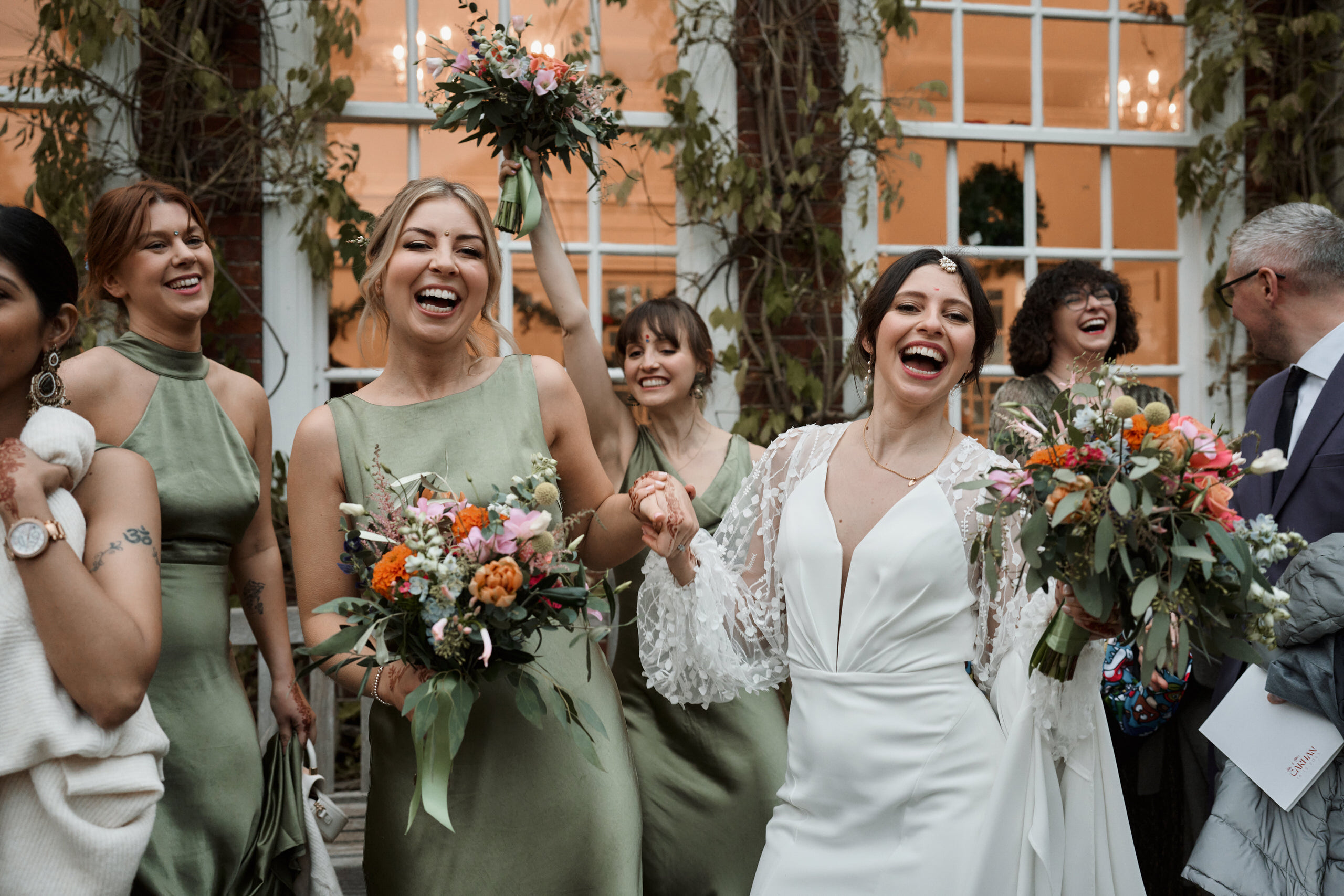 A bunch of bridesmaids are giggling and holding flower arrangements.