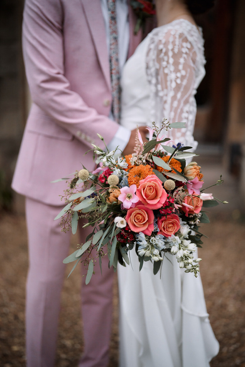 A man and woman getting married, with the man wearing a pink suit and the woman holding a bunch of flowers.