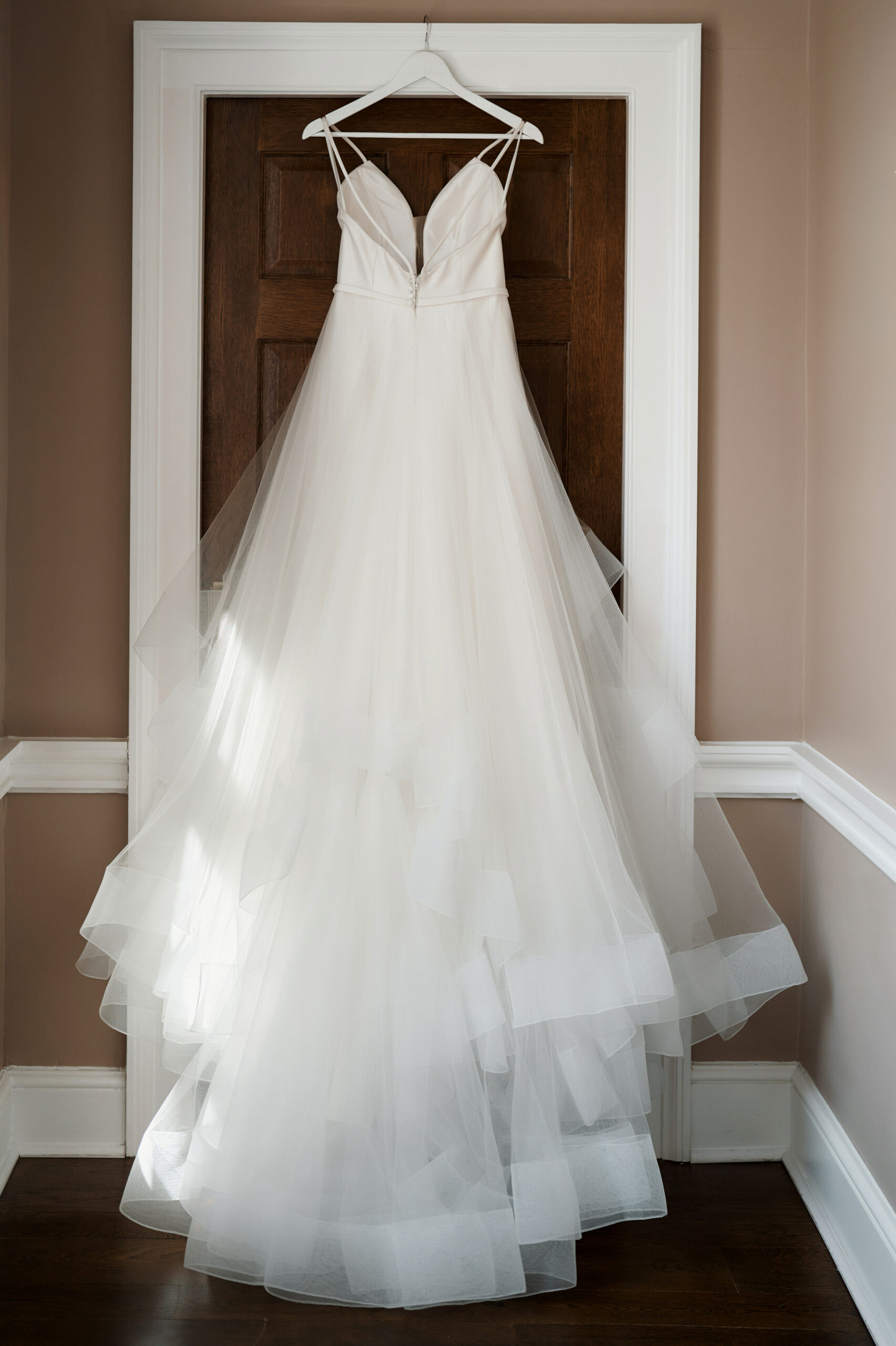 A wedding gown is hanging on a door inside a room.