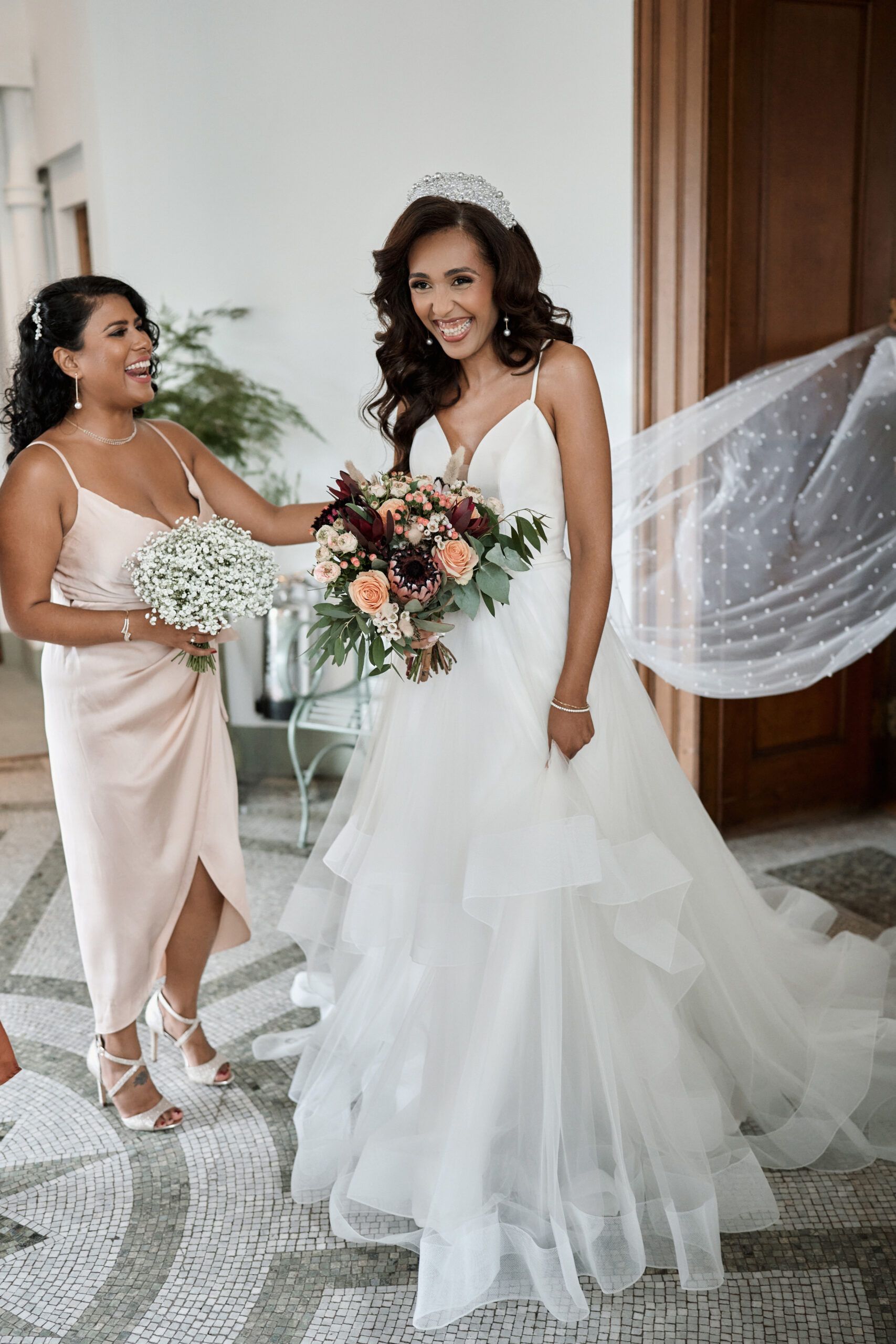 A bride and her mom are grinning at each other.