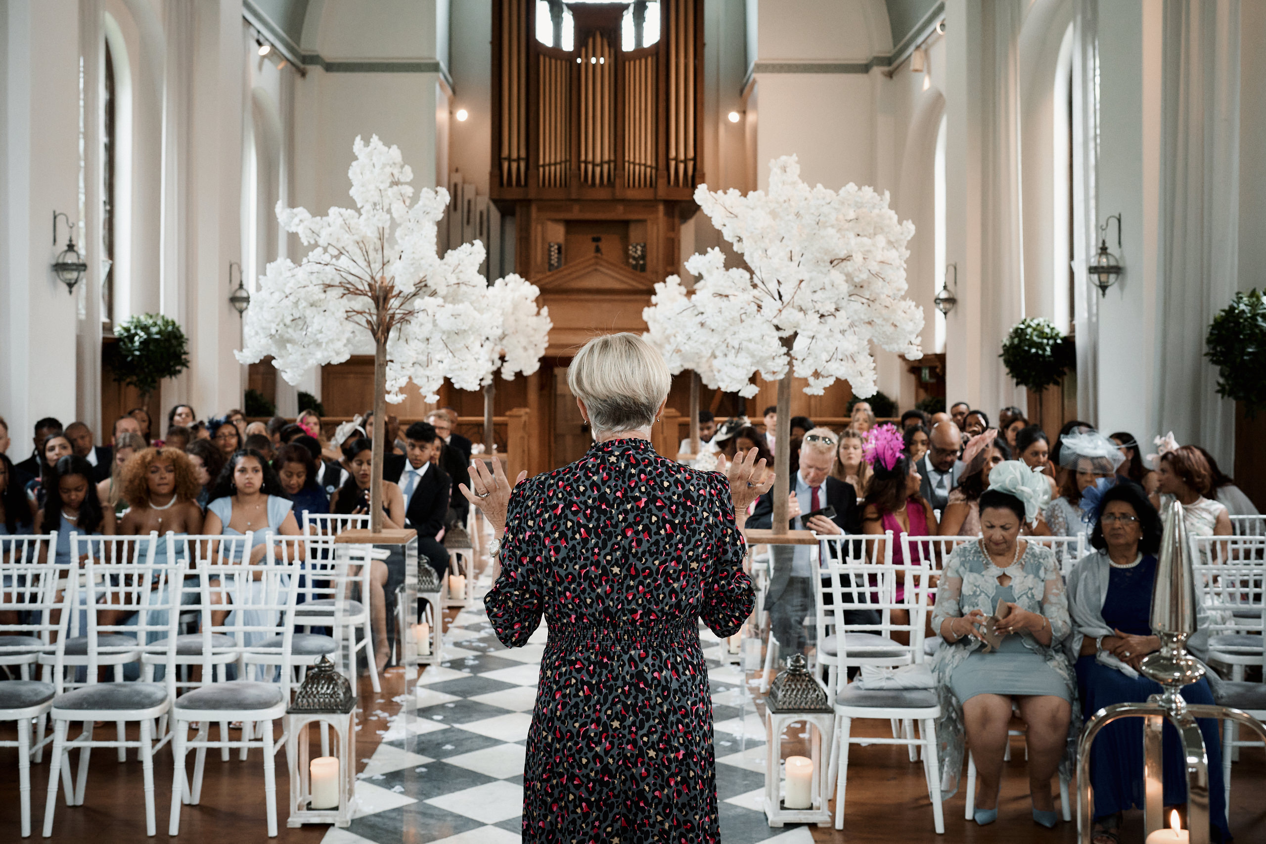 A lady standing in front of a bunch of people at a wedding.