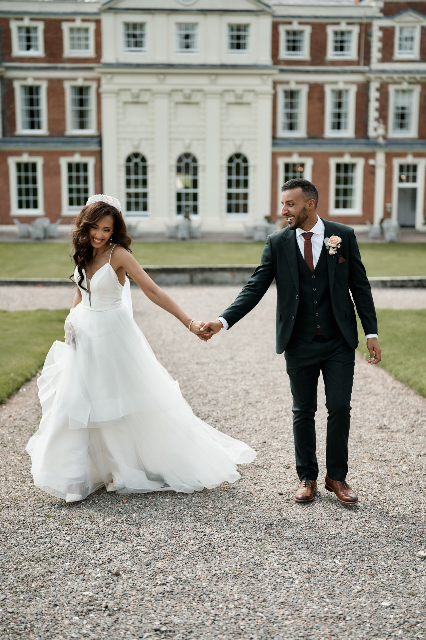 A couple getting married is holding hands in front of a big house.
