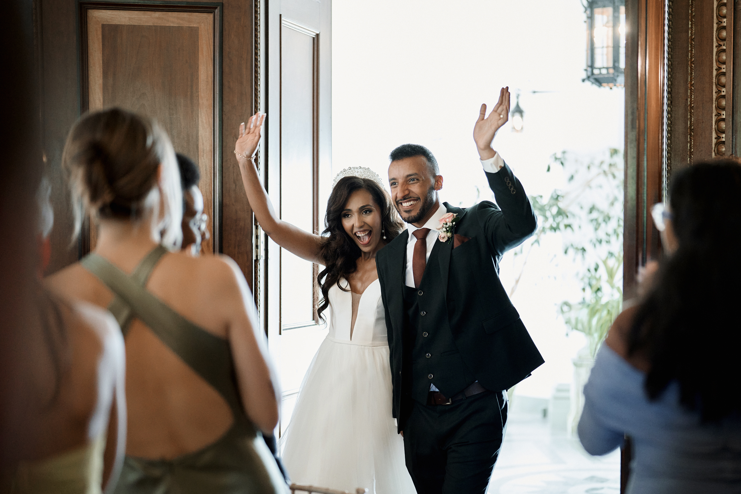 A couple getting married is waving from a room's entrance.