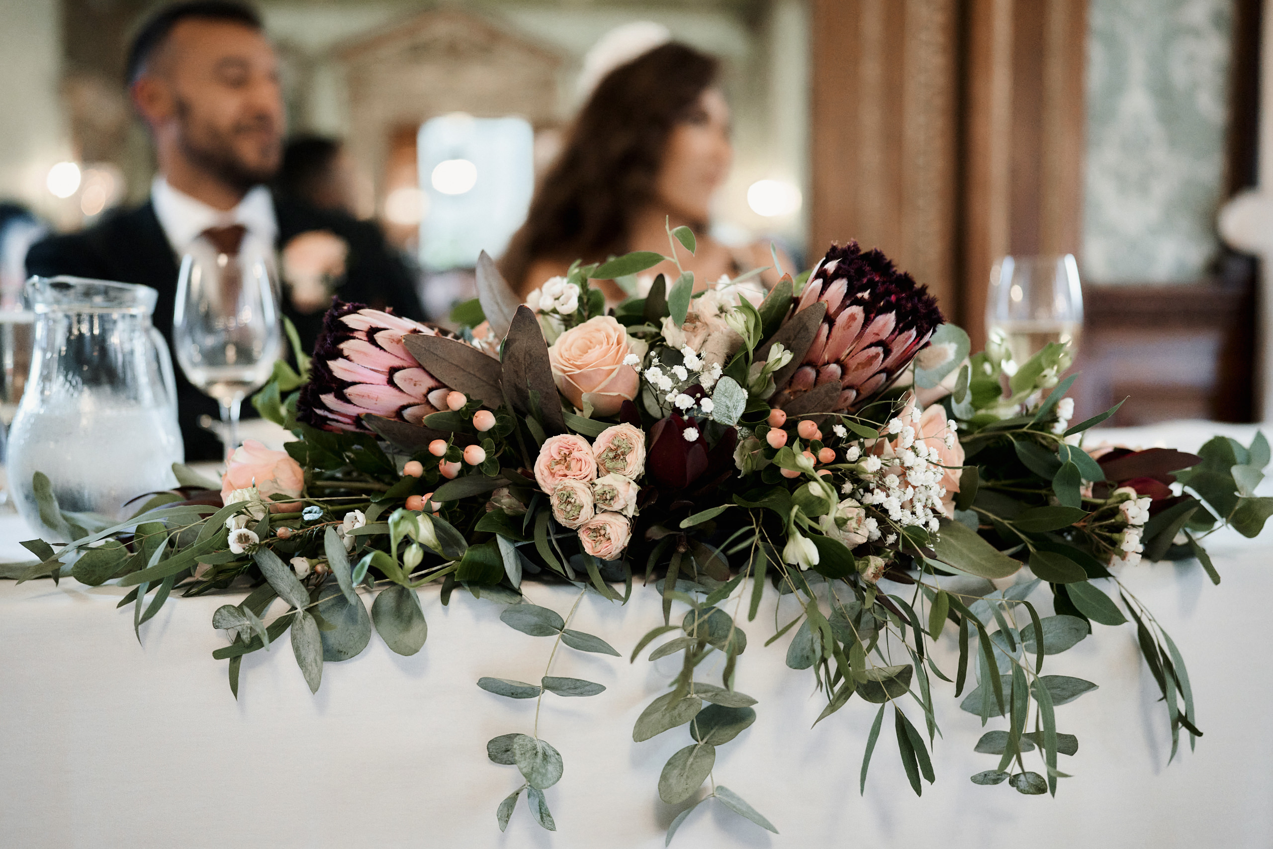 A couple getting married sitting at a table with flowers.