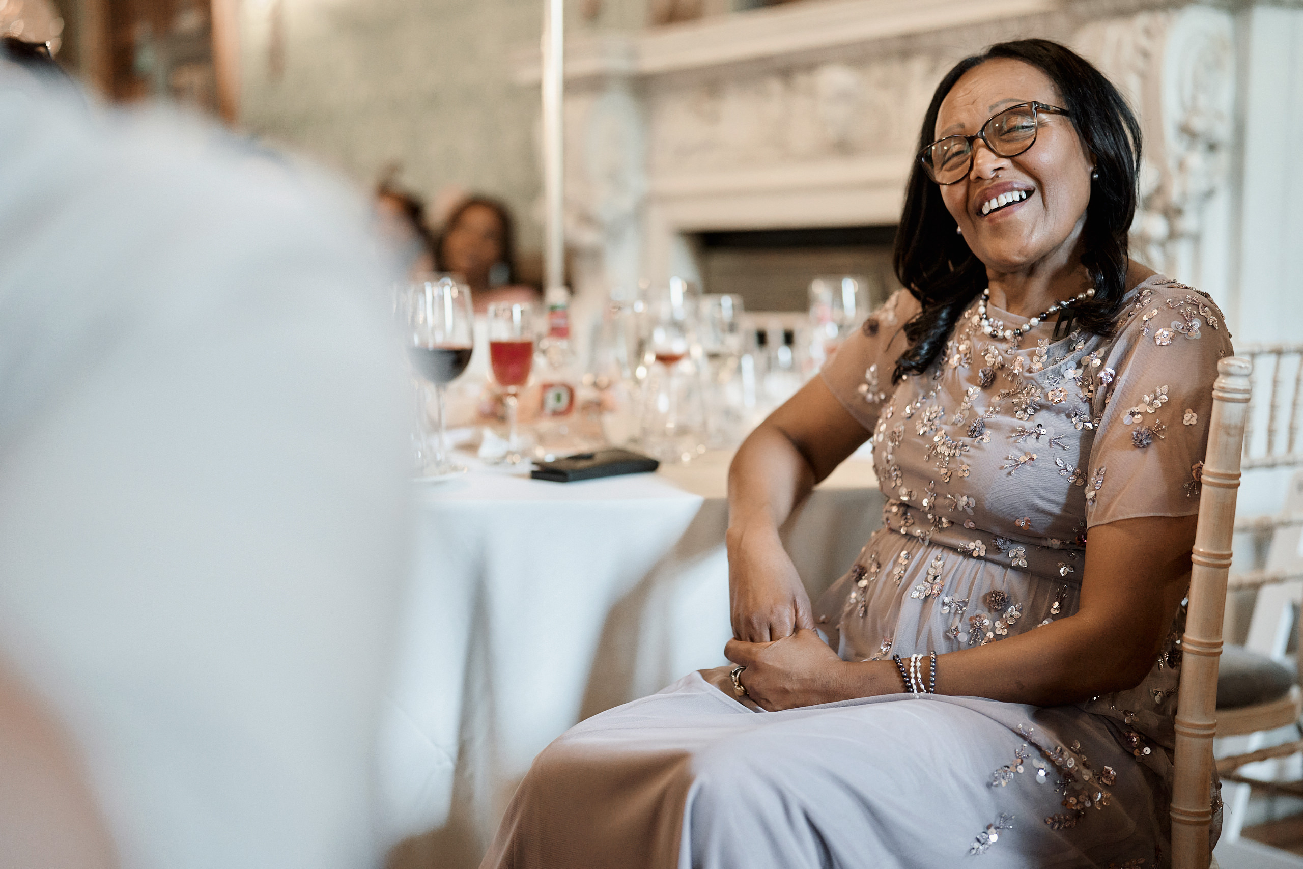A lady is grinning while seated at a table during a wedding.