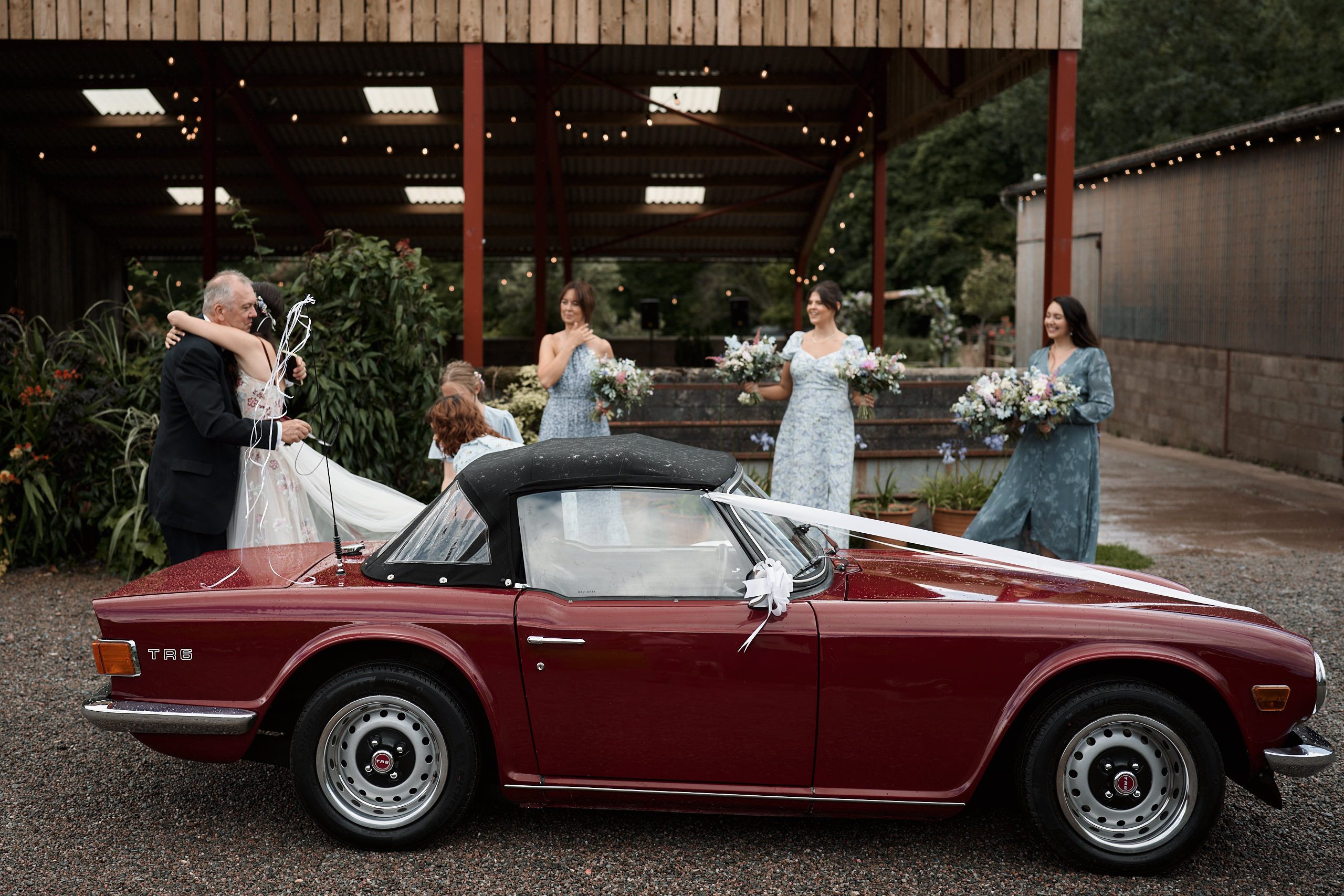 A bride and her friends are standing next to a red sports car.