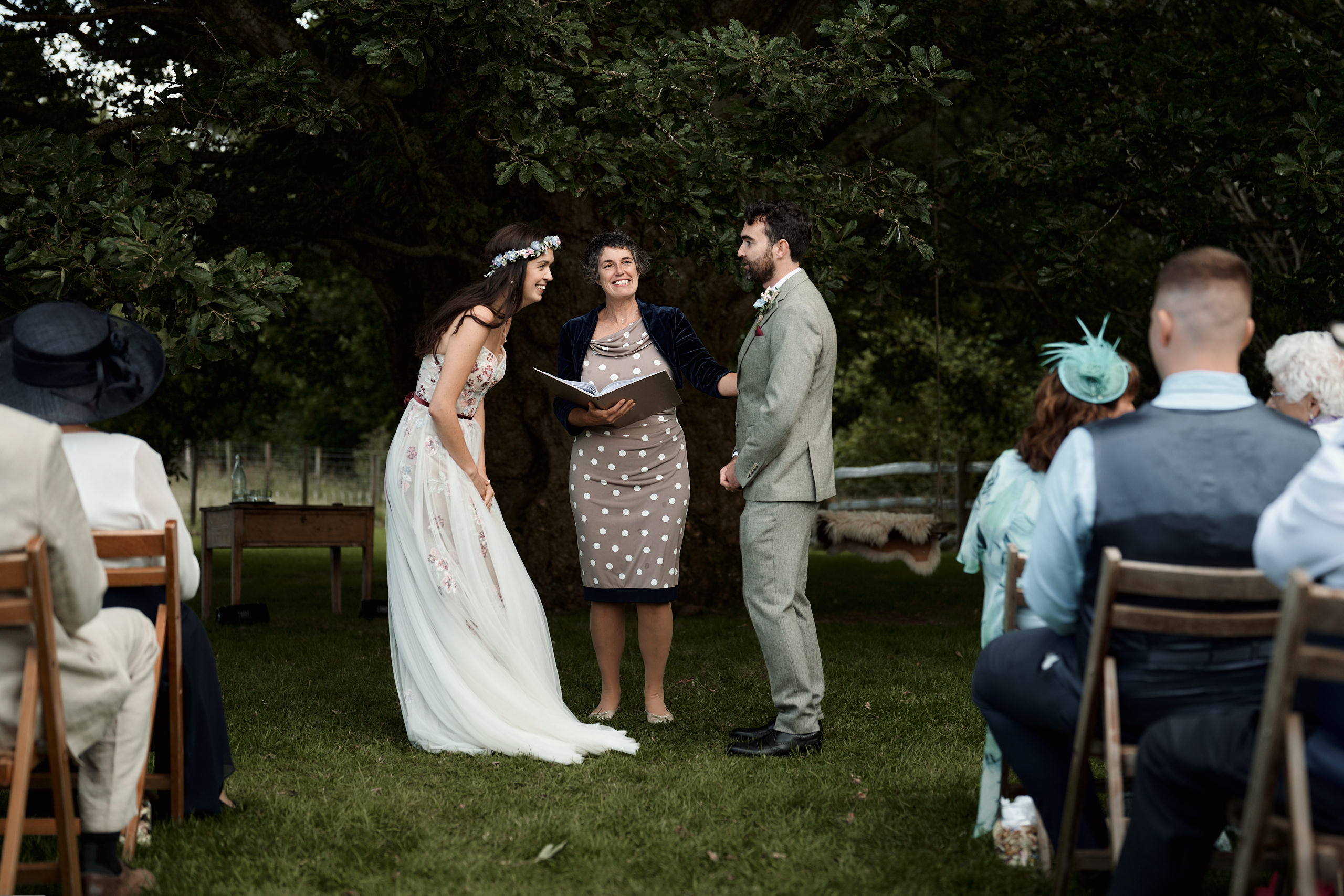A couple getting married are saying their promises to each other beneath a tree.