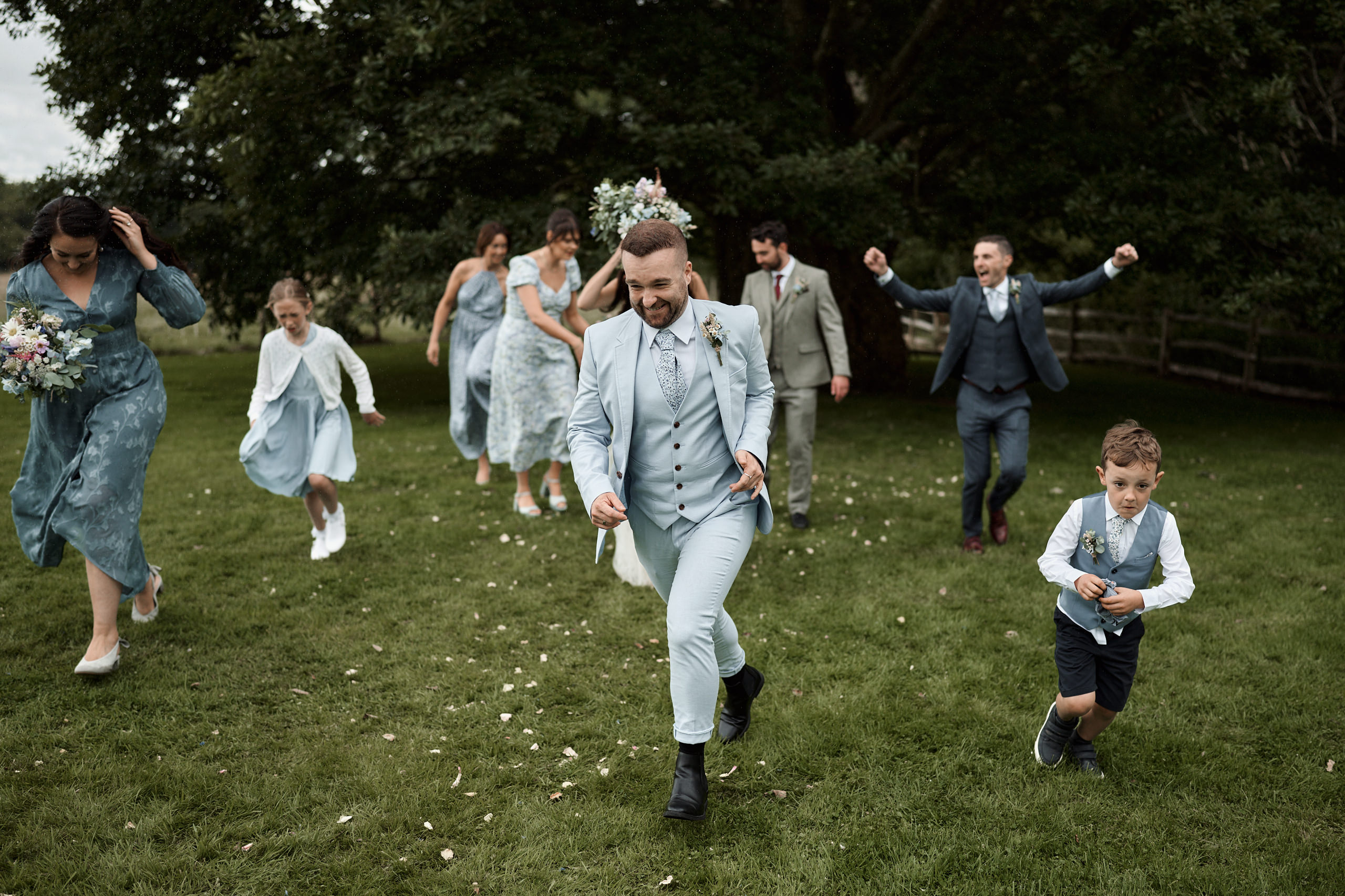 A bunch of bridesmaids and groomsmanship rushing across a field.