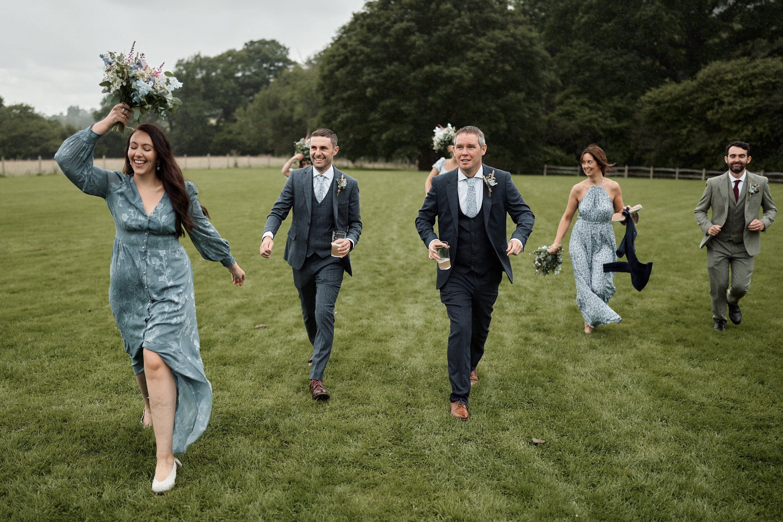 Some bridesmaids and groomsmen are running across a field.