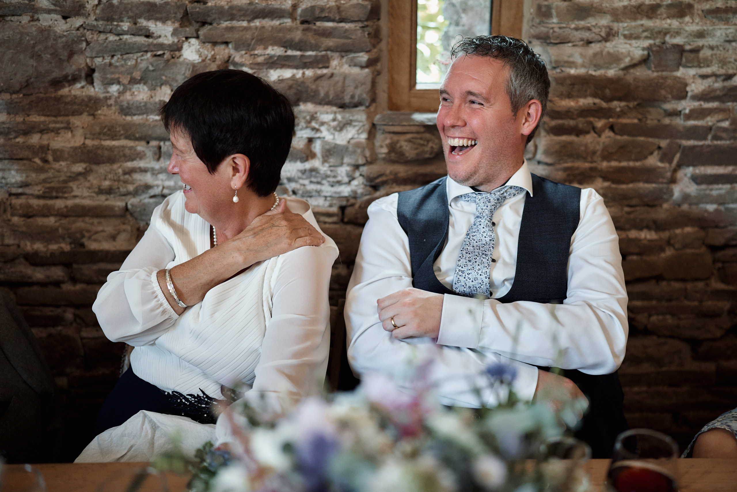 A guy and a girl cracking up at a table during a wedding.